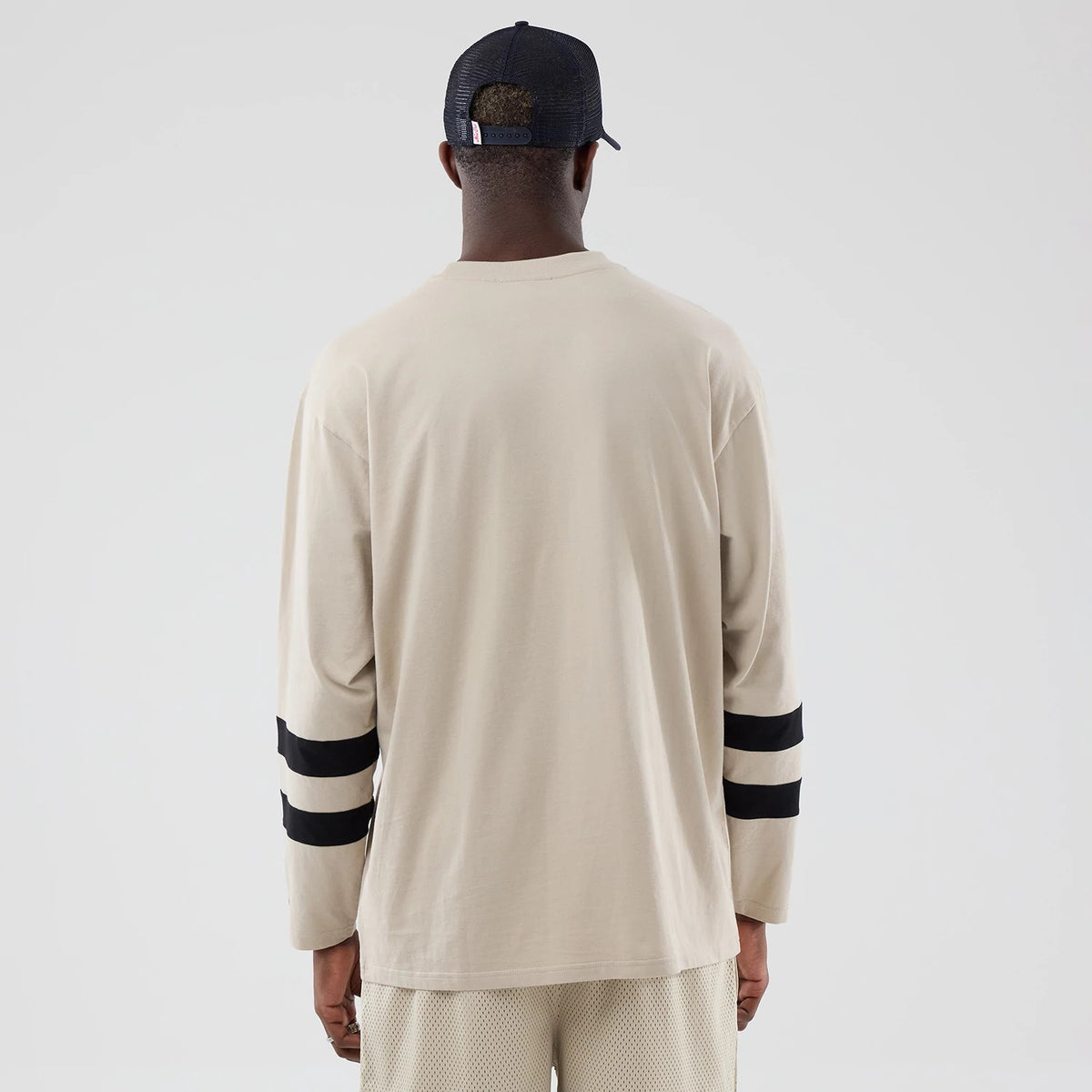 New Era New York Yankees MLB Light Beige Oversized Long Sleeve T-Shirt, back view on a model showing the plain light beige design with long sleeves, each featuring two prominent black horizontal stripes near the cuffs for a visual contrast.