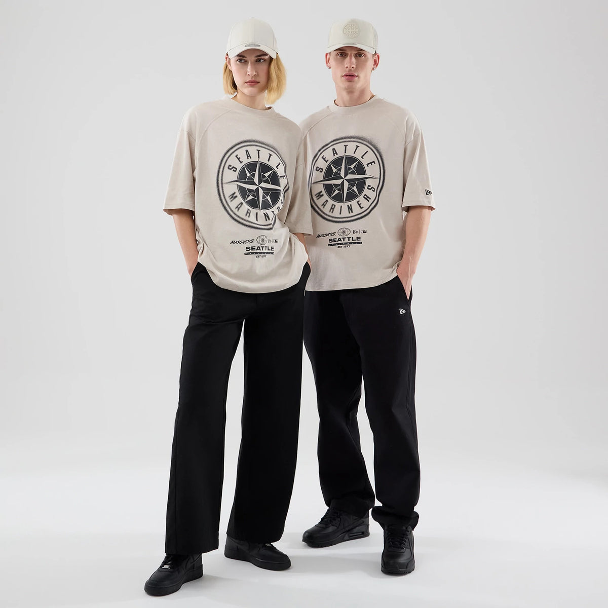 New Era Seattle Mariners MLB Graphic Cream Boxy T-Shirt, front view on models styled with matching caps, showcasing a large circular Seattle Mariners graphic in black on the front, with smaller text and a New Era embroidered logo on the left sleeve.