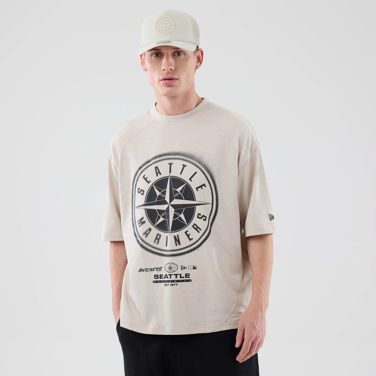 New Era Seattle Mariners MLB Graphic Cream Boxy T-Shirt, front view on a model with a matching cream cap, featuring a large circular Seattle Mariners emblem centred on the chest and a small embroidered New Era logo on the left sleeve.