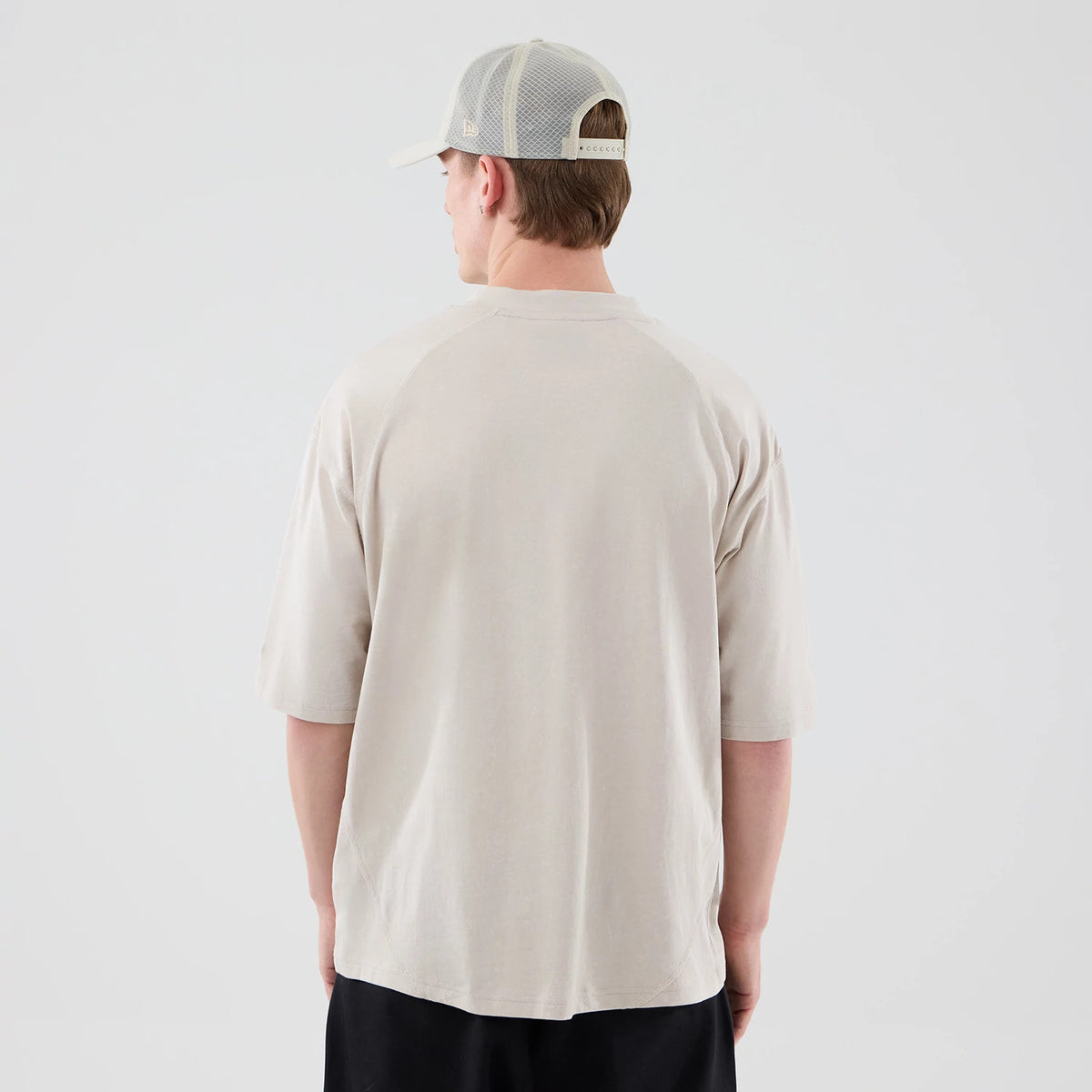 New Era Seattle Mariners MLB Graphic Cream Boxy T-Shirt, back view on a model wearing a grey cap and black trousers, the plain cream back of the shirt with raglan sleeves and a slightly loose.