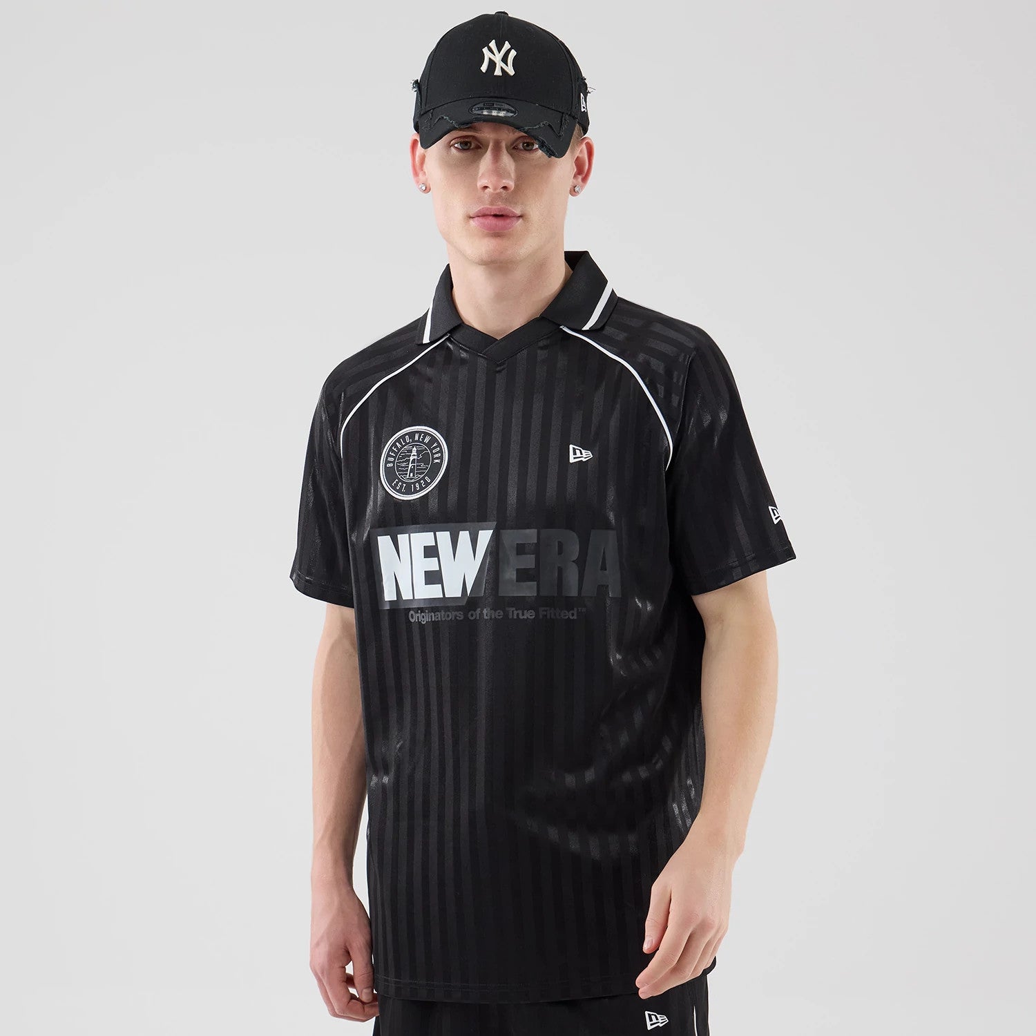 New Era Black Football Jersey T-Shirt, front view on-model showing a black shirt with vertical stripes, a prominent white NEW ERA logo across the chest, an embroidered circular emblem on the upper right side.
