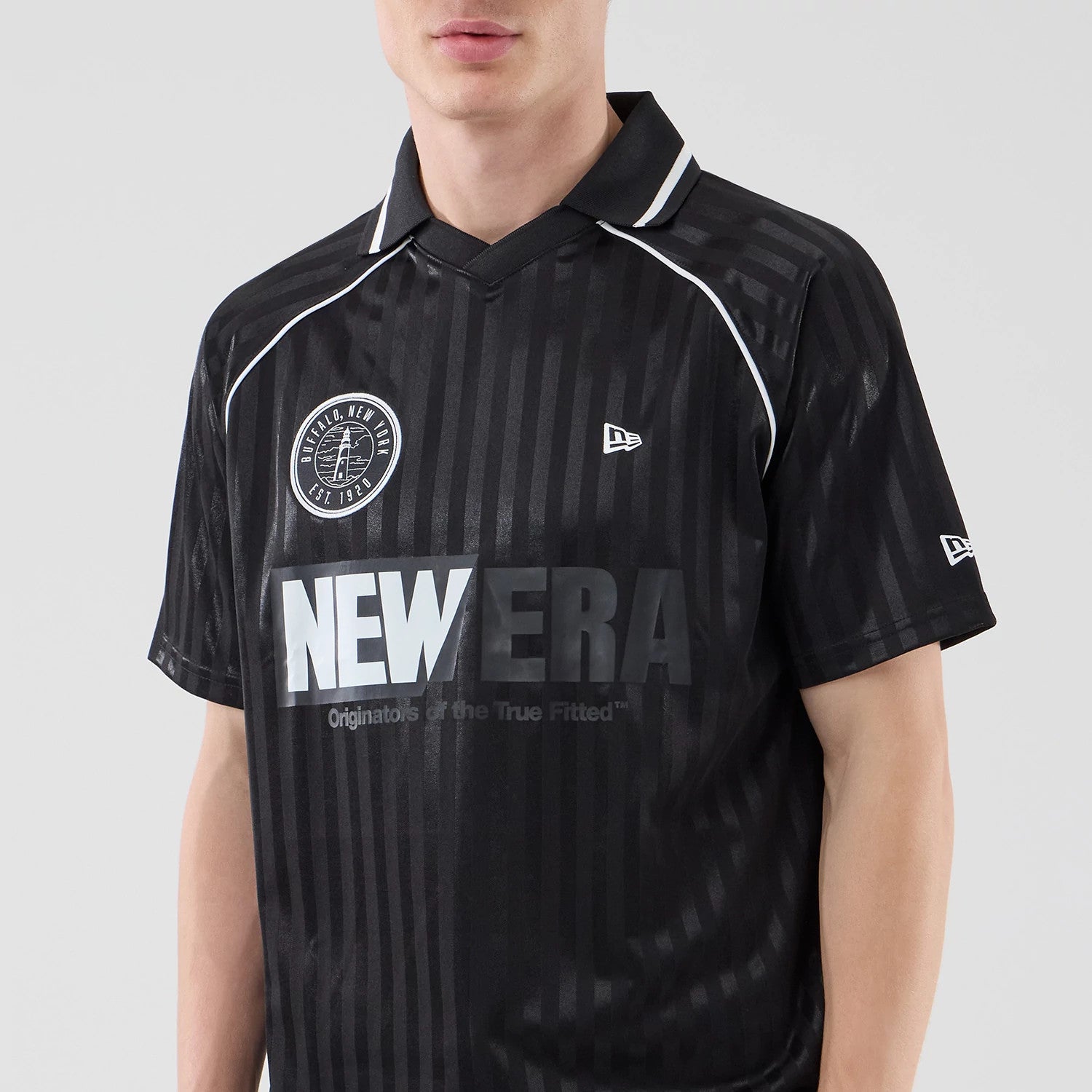 New Era Black Football Jersey T-Shirt, front view on a model featuring NEW ERA lettering across the chest, a circular embroidered logo on the upper left, white piping along the shoulders, and small embroidered logos on the sleeves.