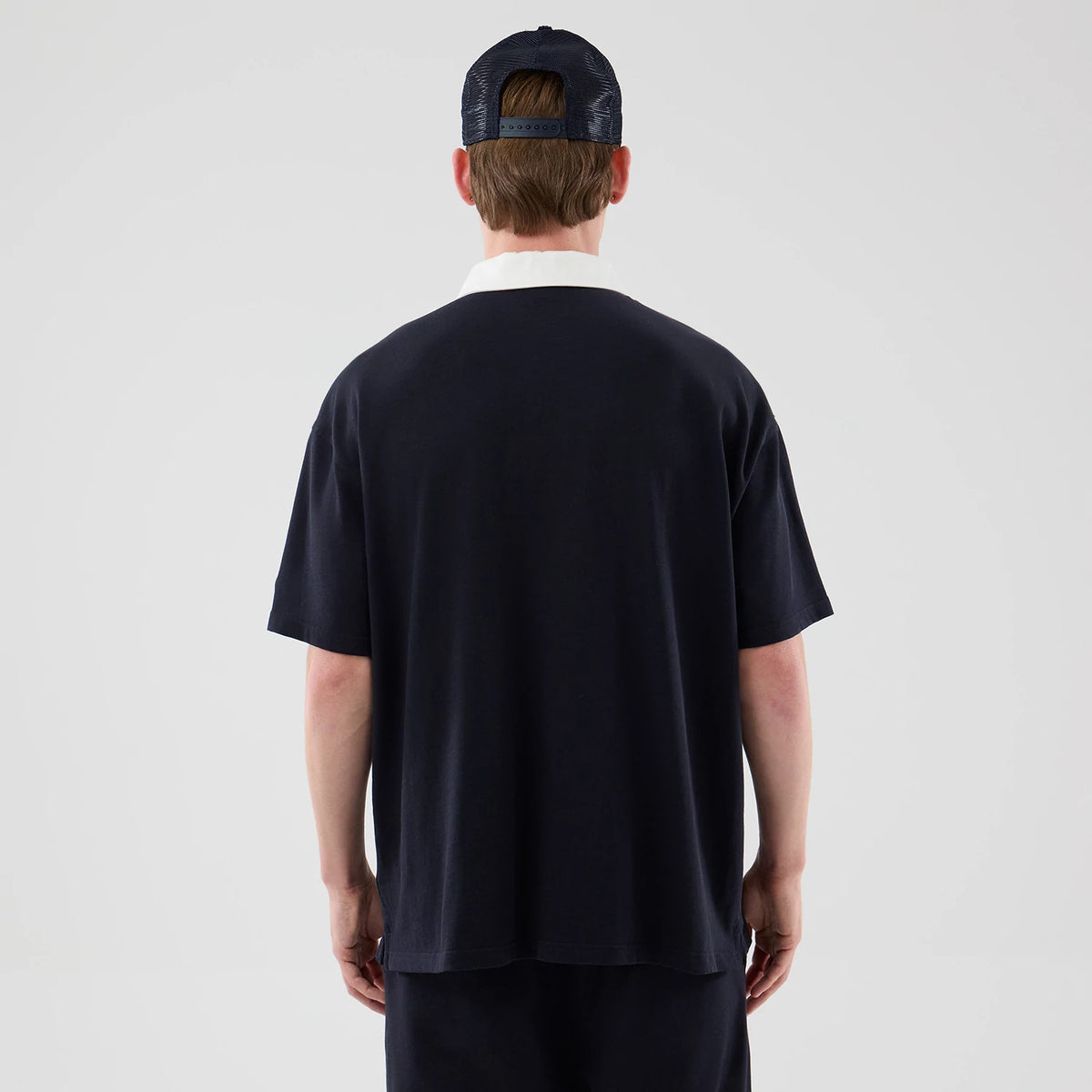 New Era New York Yankees MLB Navy Polo T-Shirt, back view on a model wearing a navy cap, featuring a plain navy back with short sleeves and a contrast white collar, showcasing the relaxed fit of the polo shirt.