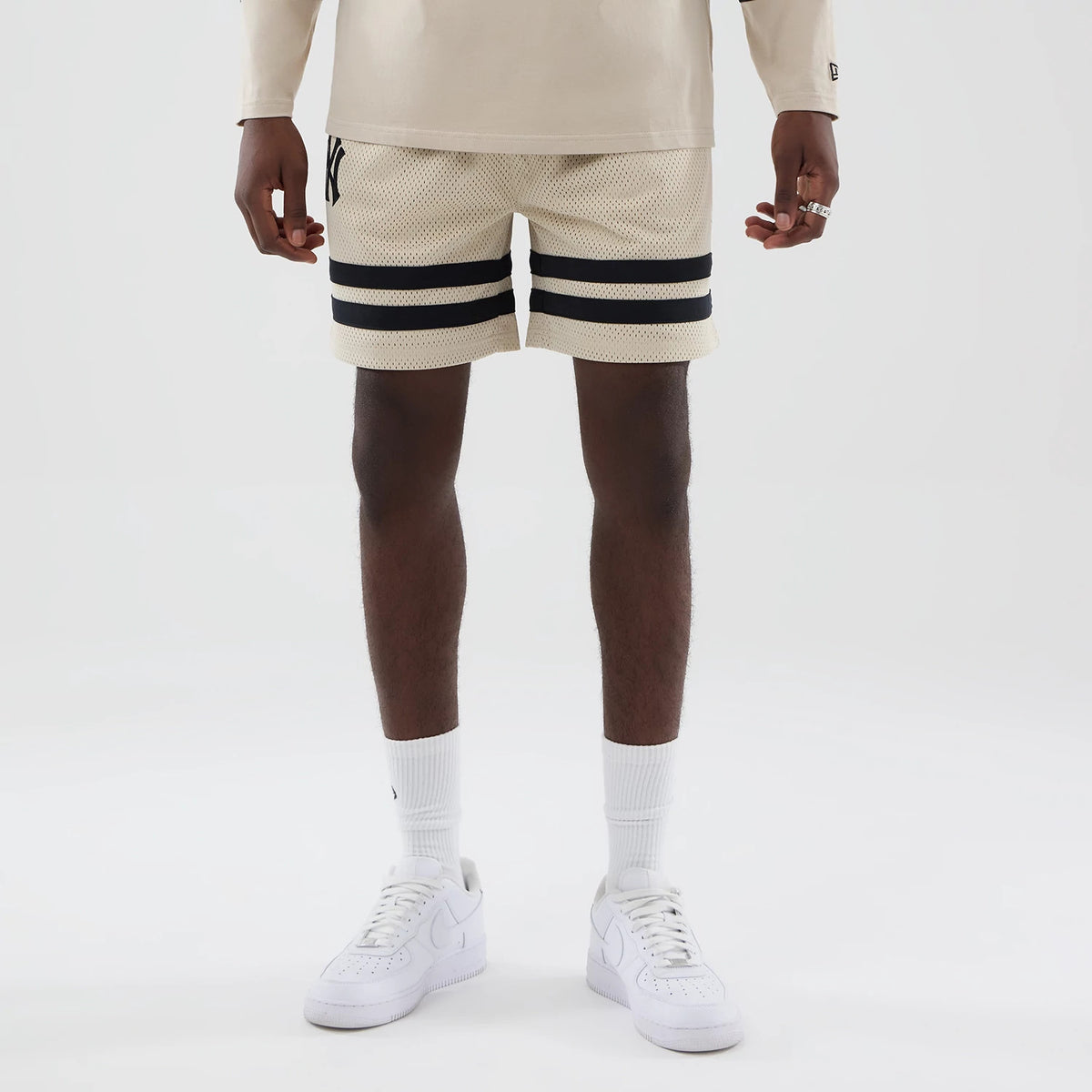 New Era New York Yankees MLB Light Beige Oversized Mesh Shorts, front view featuring an embroidered New York Yankees logo on the upper left thigh, two black horizontal stripes near the hem.