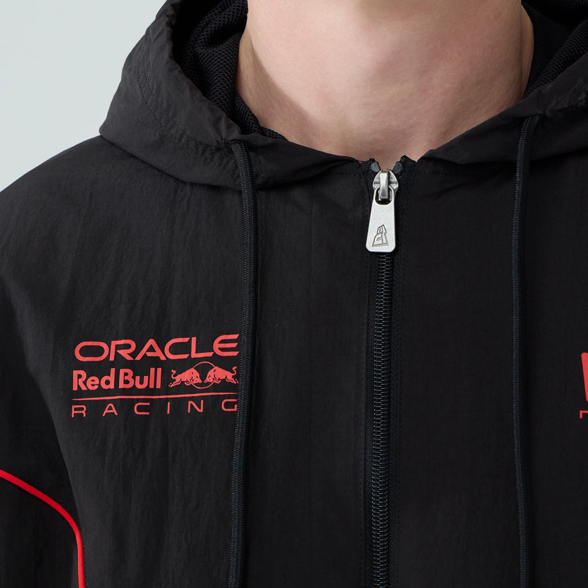 New Era Red Bull Racing Piping Black Track Jacket, front view showing a model wearing the jacket with a close-up of the zip, an embroidered Oracle Red Bull Racing logo in red on the chest, and a red piping detail along the shoulder.