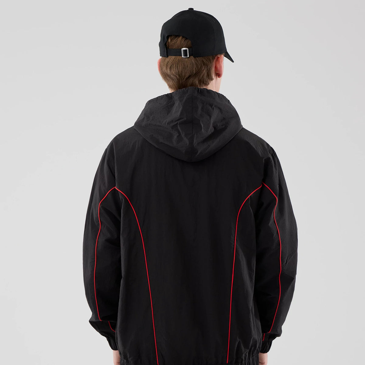 New Era Red Bull Racing Piping Black Track Jacket, back view on a model showing the hooded design with distinctive red piping running down the sleeves and sides, complemented by a relaxed fit with gathered cuffs and hem.