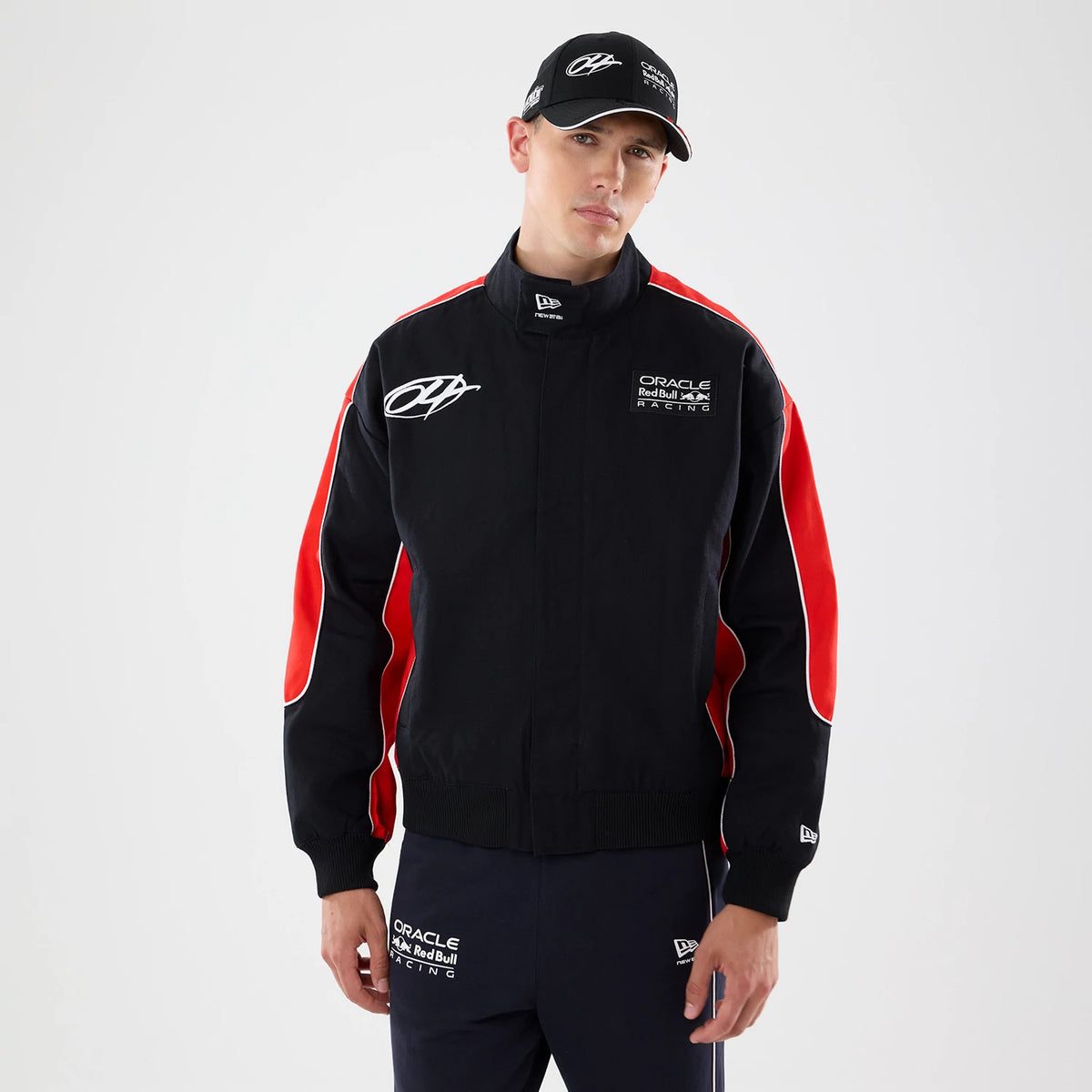 New Era Red Bull Racing Motorsport Black Jacket, front view on a model paired with a matching cap, featuring embroidered white Red Bull Racing lettering on the chest, red stripes along the sleeves, and an embroidered logo on the right chest.