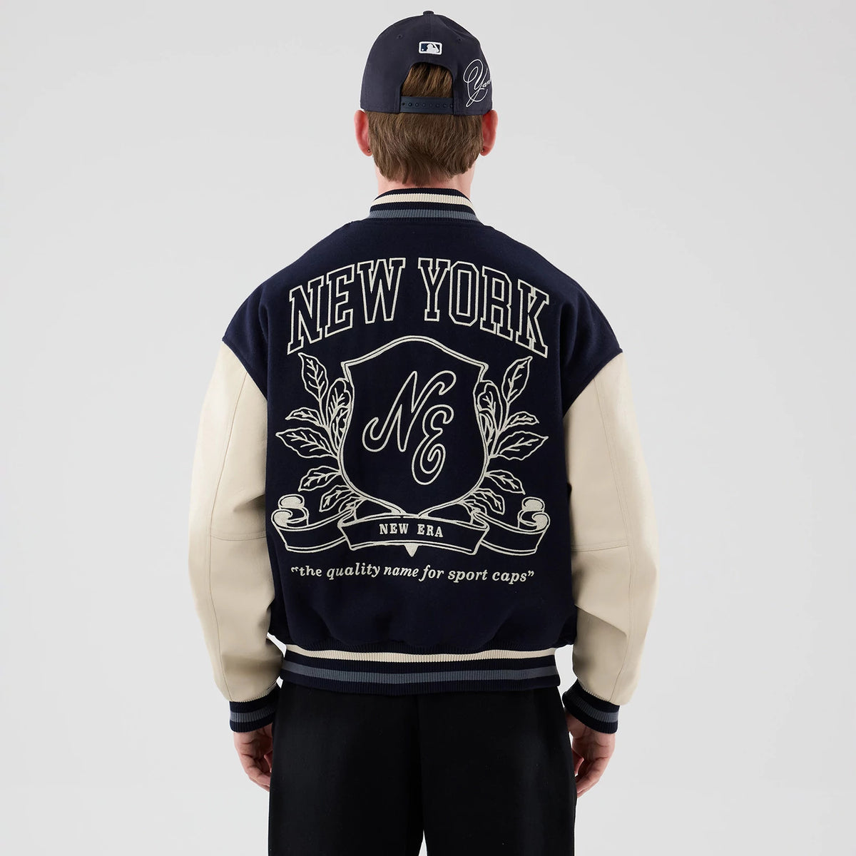 The model is wearing this New Era Oversized Varsity Jacket in navy. 2
