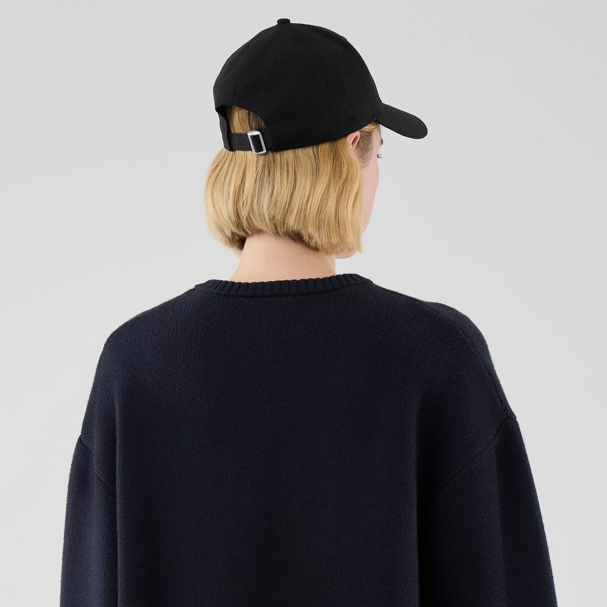 New Era Knit Script Navy Knitted Sweater, back view on a model with a black cap, featuring a ribbed crewneck and long, slightly dropped sleeves, highlighting the navy texture of the knit.