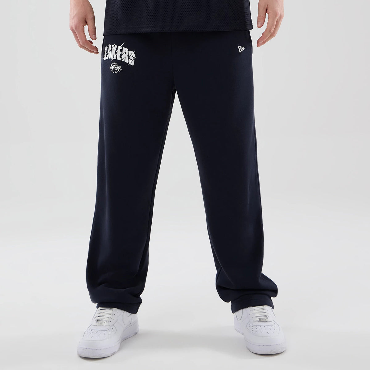 New Era LA Lakers NBA Core Plus Navy Straight Leg Joggers, front view on a model with white sneakers, showing the white Lakers lettering and logo on the upper left leg, along with the New Era flag logo on the right side.