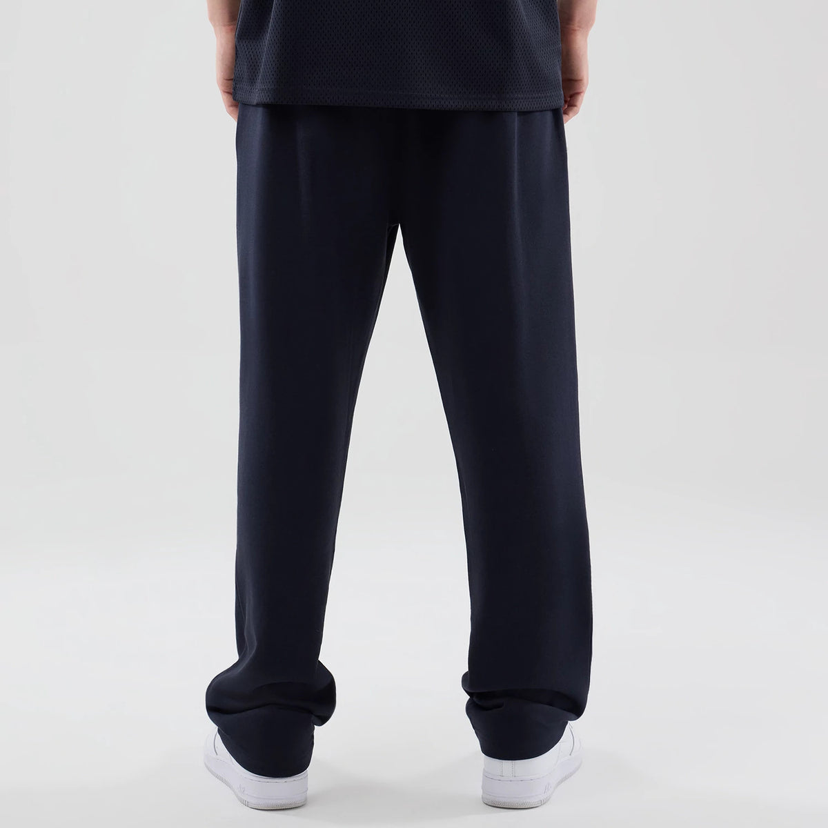 New Era LA Lakers NBA Core Plus Navy Straight Leg Joggers, rear view on a model showing the navy straight leg design with a relaxed fit, cuffed hems resting over white trainers, and a mesh texture on the upper garment.