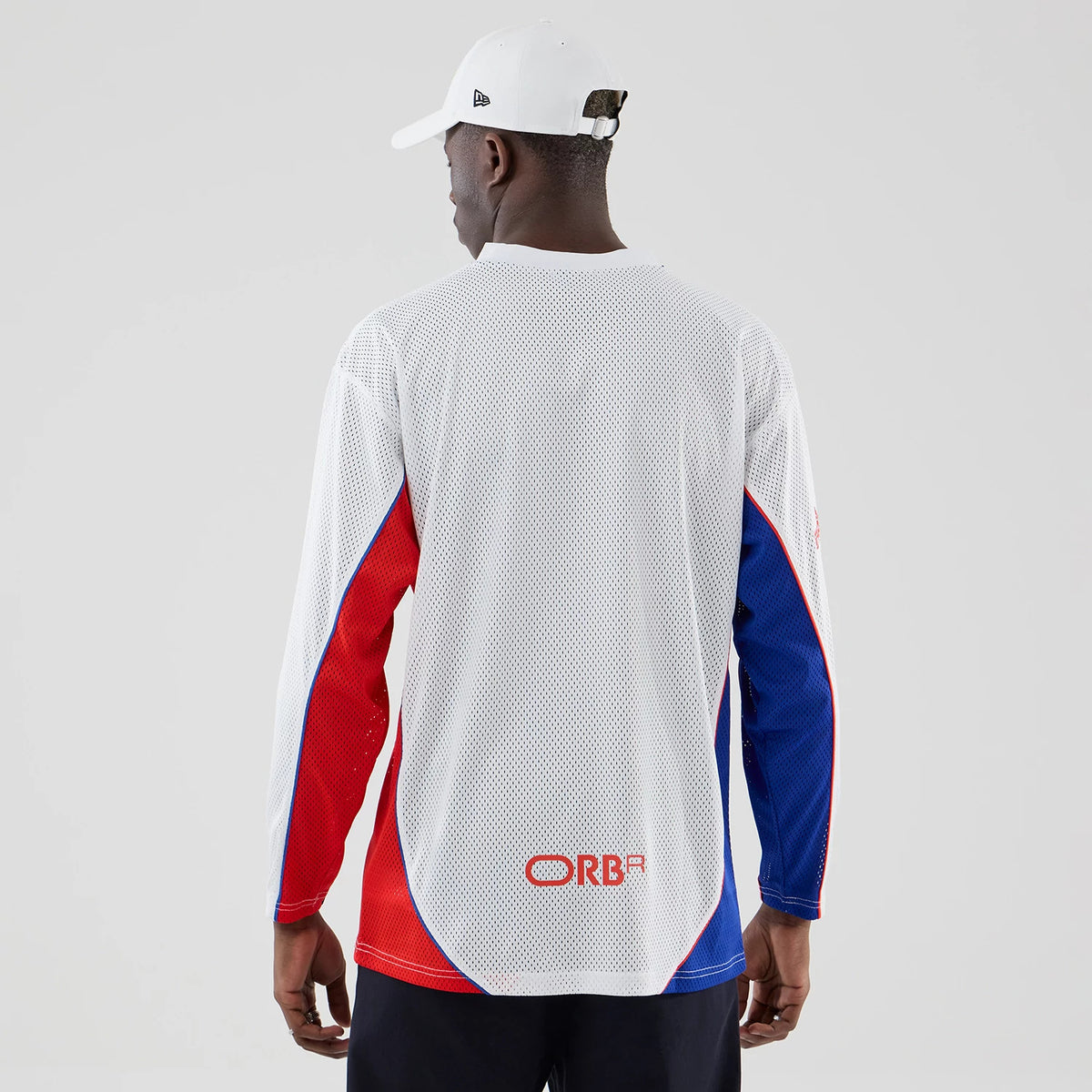 New Era Red Bull Racing White Hockey Jersey, back view on a model with distinctive red and blue panels on the sleeves, ribbed neckline, and the ORBR logo printed in red on the lower back of the white mesh fabric.