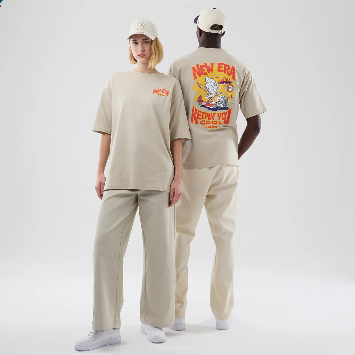 New Era Food Graphic Light Beige Oversized T-Shirt, front and back view on models showing the embroidered New Era logo on the left chest and a large colourful graphic on the back with Keepin' You Cool lettering surrounded by animated food characters.
