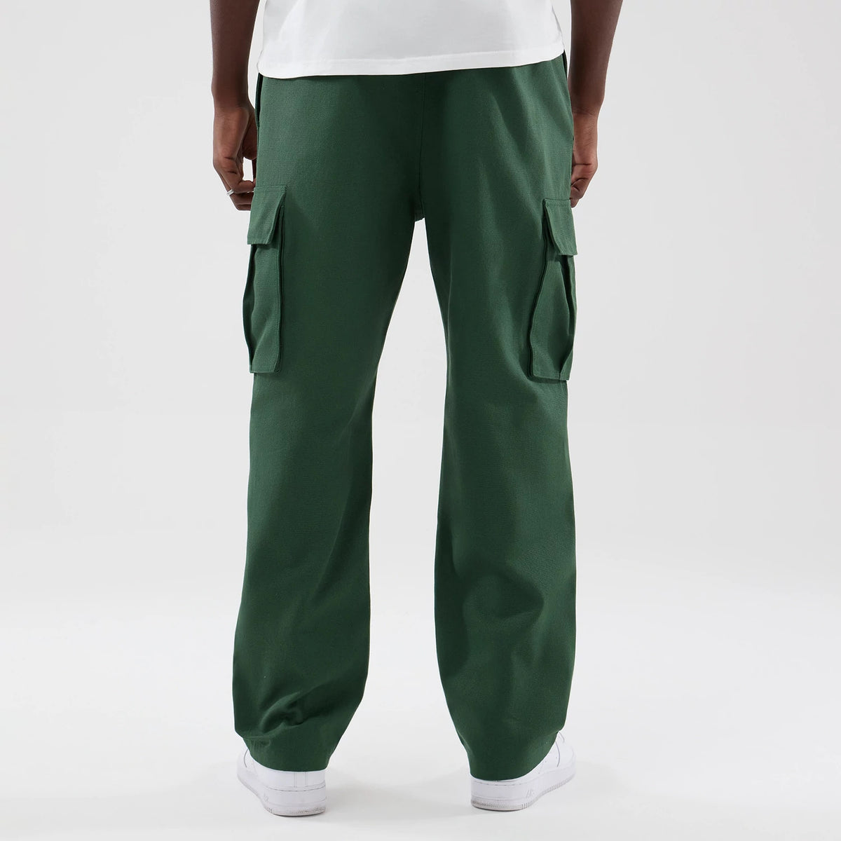 New Era Dark Green Cargo Trousers, rear view on a model showing the deep green colour, two large flap pockets on the thighs, and a loose straight-leg fit resting on white trainers.