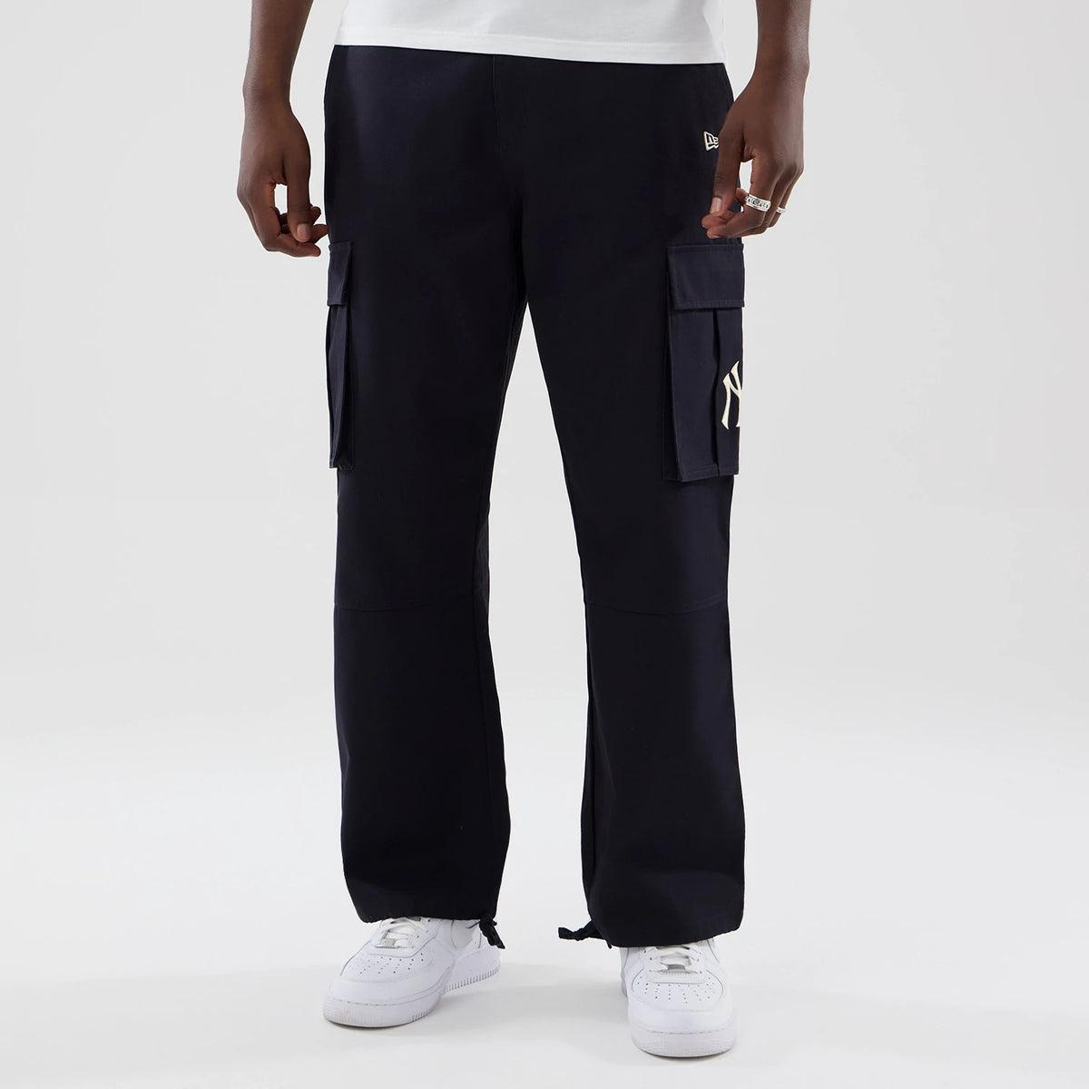 New Era New York Yankees MLB Navy Cargo Trousers, front view on a model showing the NY logo on the right cargo pocket, New Era flag logo above the left pocket, and adjustable drawstring hems with a relaxed fit over white trainers.