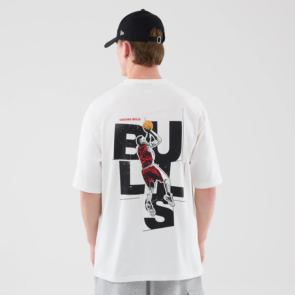 New Era Chicago Bulls NBA Player Graphic White Oversized T-Shirt, back view on a model showing a prominent black BU LLS lettering across the back with a red and white graphic of an NBA player in action, and small CHICAGO BULLS text above.