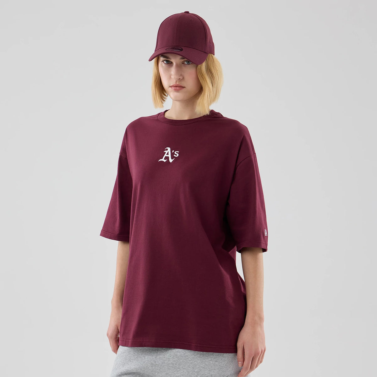New Era Athletics MLB Midi League Essential Dark Red Oversized T-Shirt, front view on a model with a dark red cap, showcasing the white embroidered A's logo on the chest and a small New Era logo embroidered on the left sleeve.
