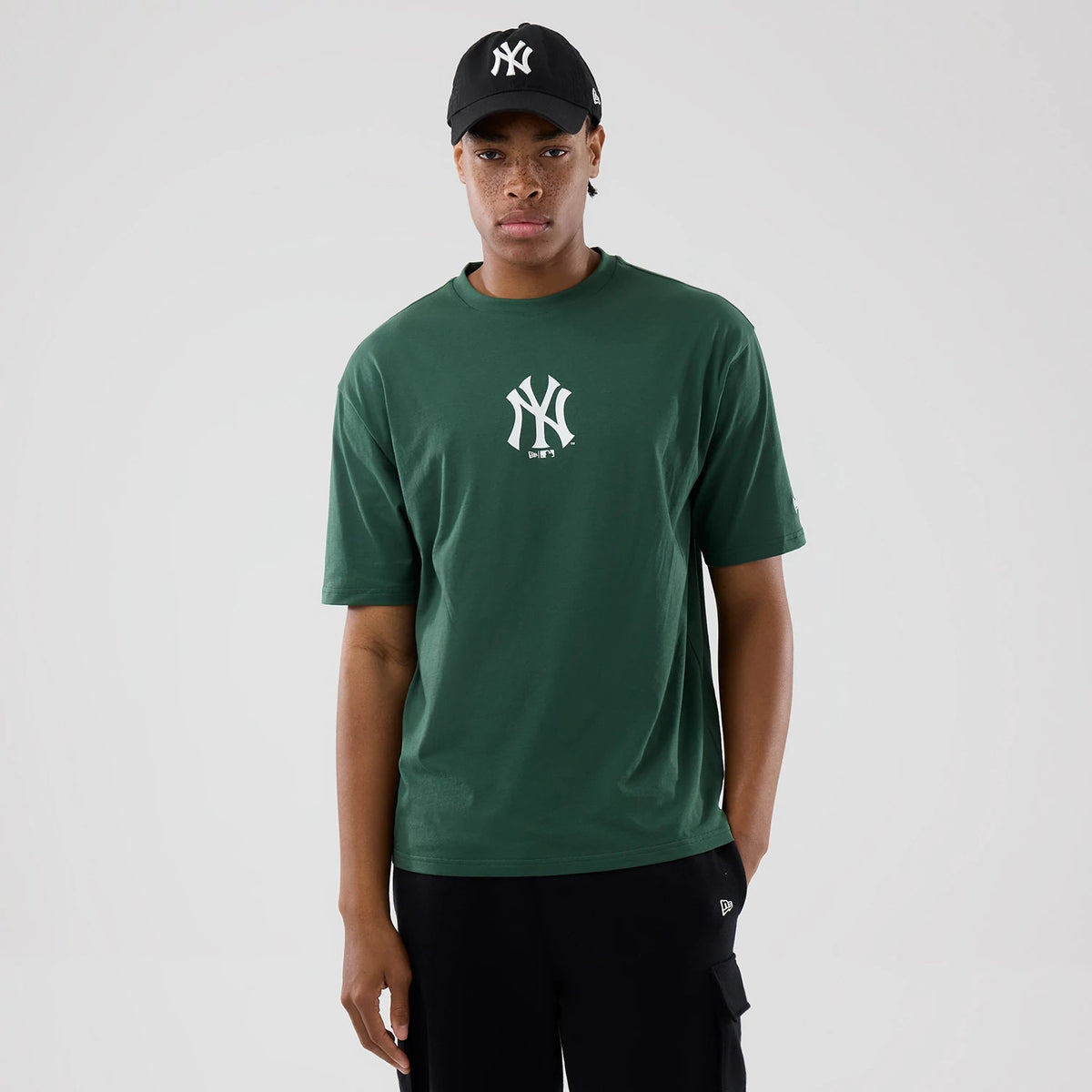 New Era New York Yankees MLB Food Graphic Dark Green Oversized T-Shirt, front view on a model styled with a black cap, showcasing the white printed Yankees logo centrally on the chest and a small printed New Era logo on the left sleeve.