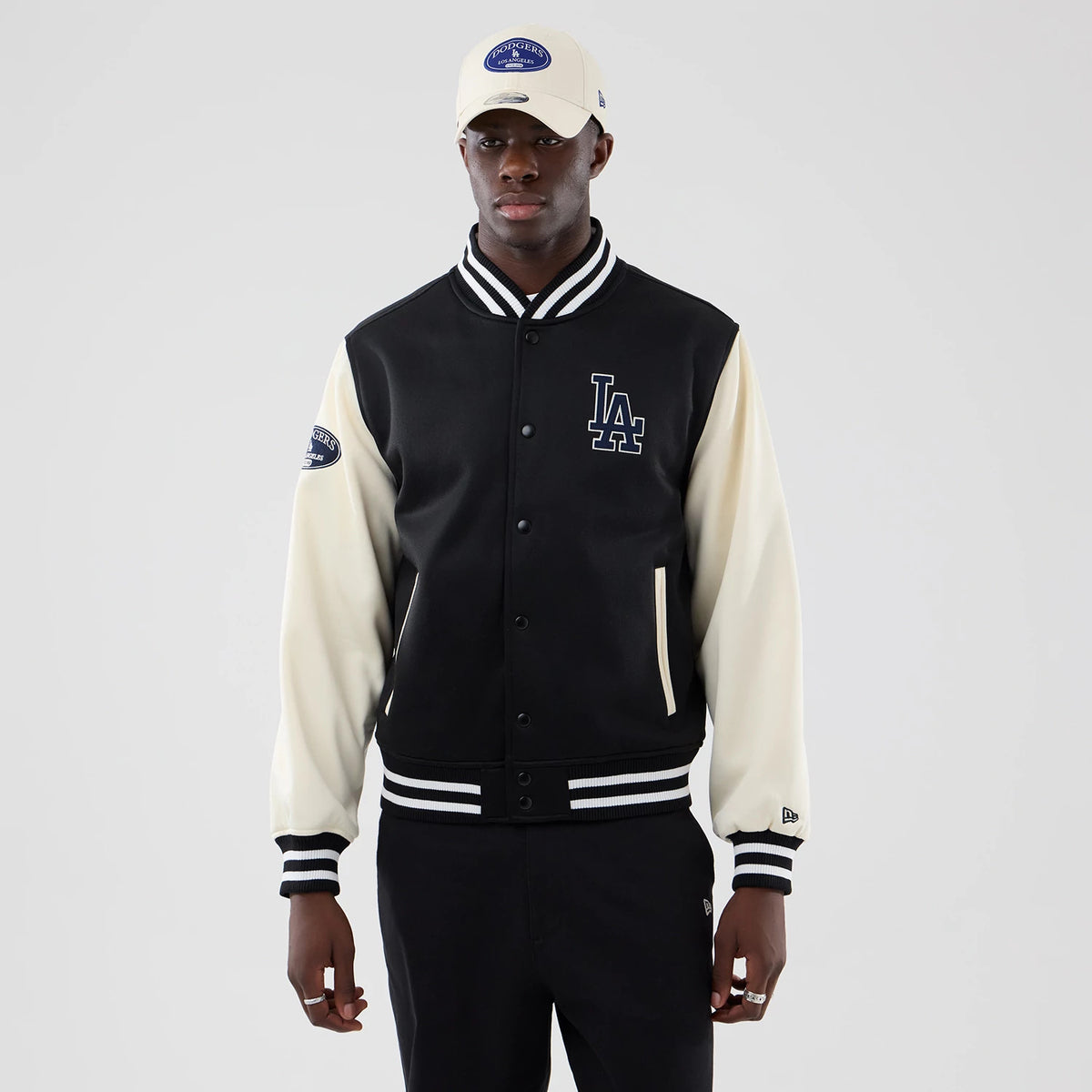 New Era LA Dodgers MLB Jersey Bomber Black Jacket, front view on-model showing the black and cream sleeves with black embroidered LA logo on the left chest, team patch on the right sleeve, and striped black and white cuffs and waistband.