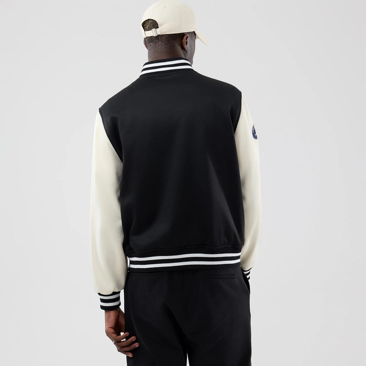 New Era LA Dodgers MLB Jersey Bomber Black Jacket, back view on a model wearing a beige cap, showing the contrasting white sleeves, a striped collar, cuffs and hem, and an embroidered logo patch on the left sleeve.