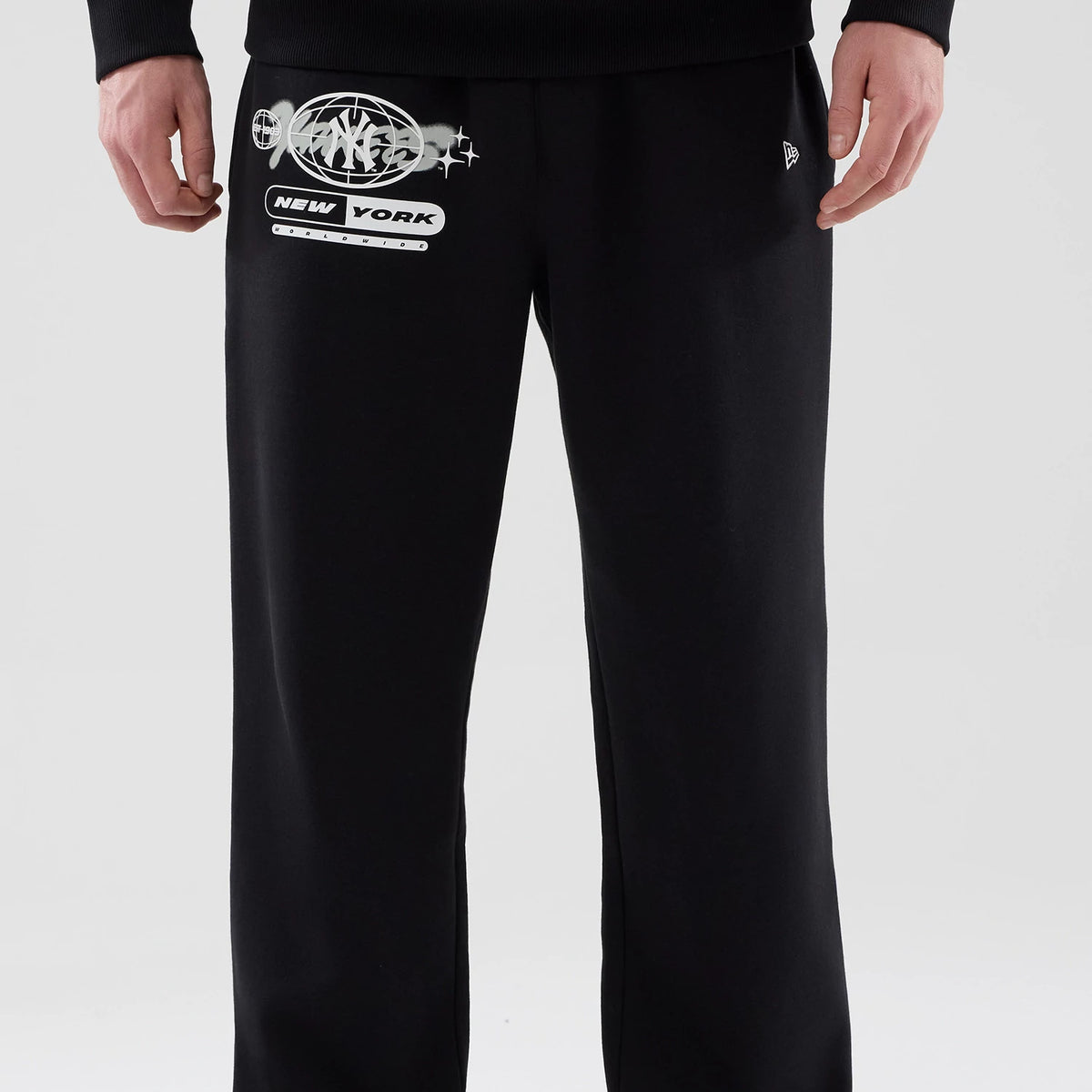New Era New York Yankees MLB Logo Graphic Black Straight Leg Joggers, front view on a model featuring a large grey and white Yankees graphic with stars on the left thigh, a small embroidered New Era flag logo on the right side.