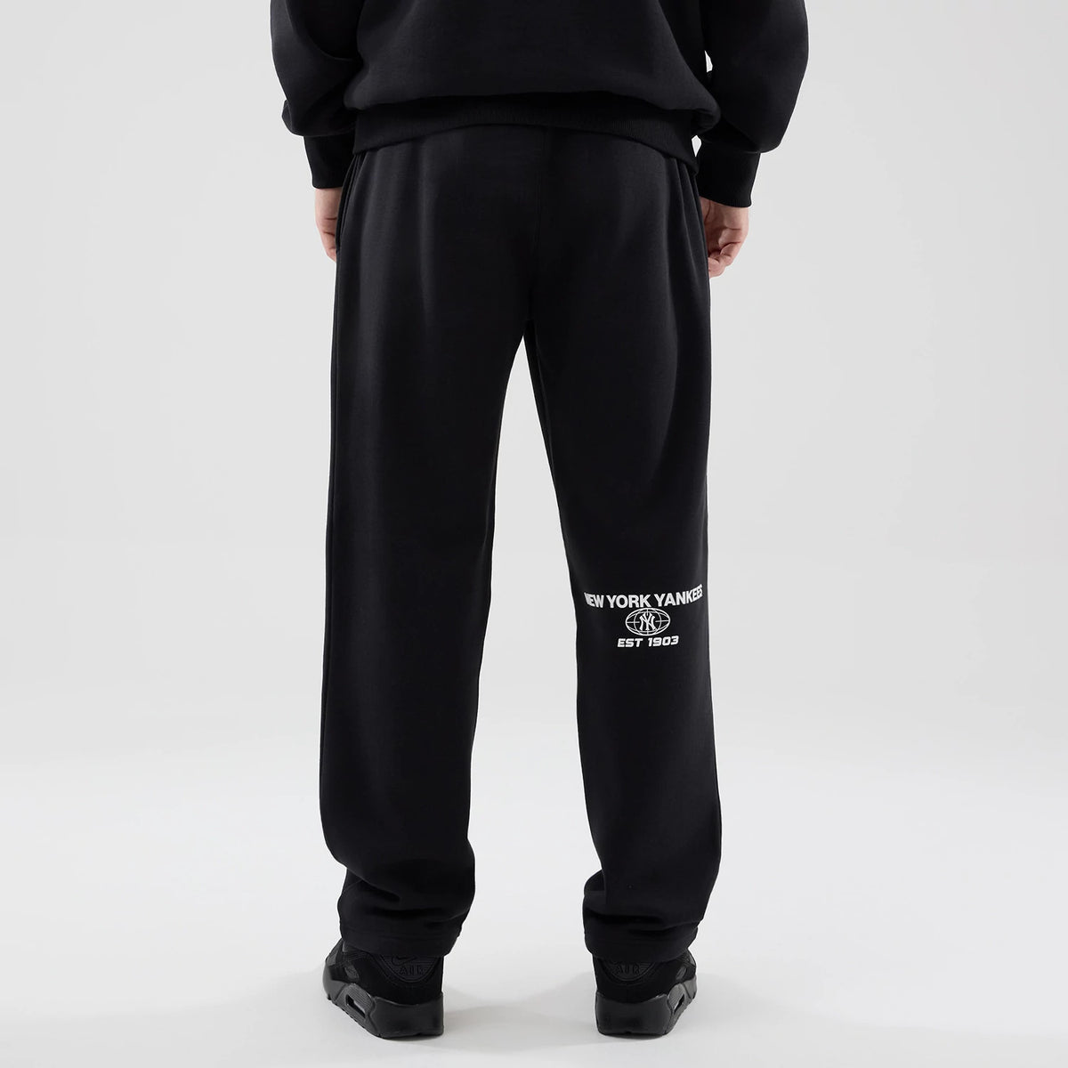 New Era New York Yankees MLB Logo Graphic Black Straight Leg Joggers, rear view on a model showing the white New York Yankees logo with 'Est 1903' under it on the left leg, and an elastic waistband with a relaxed fit.