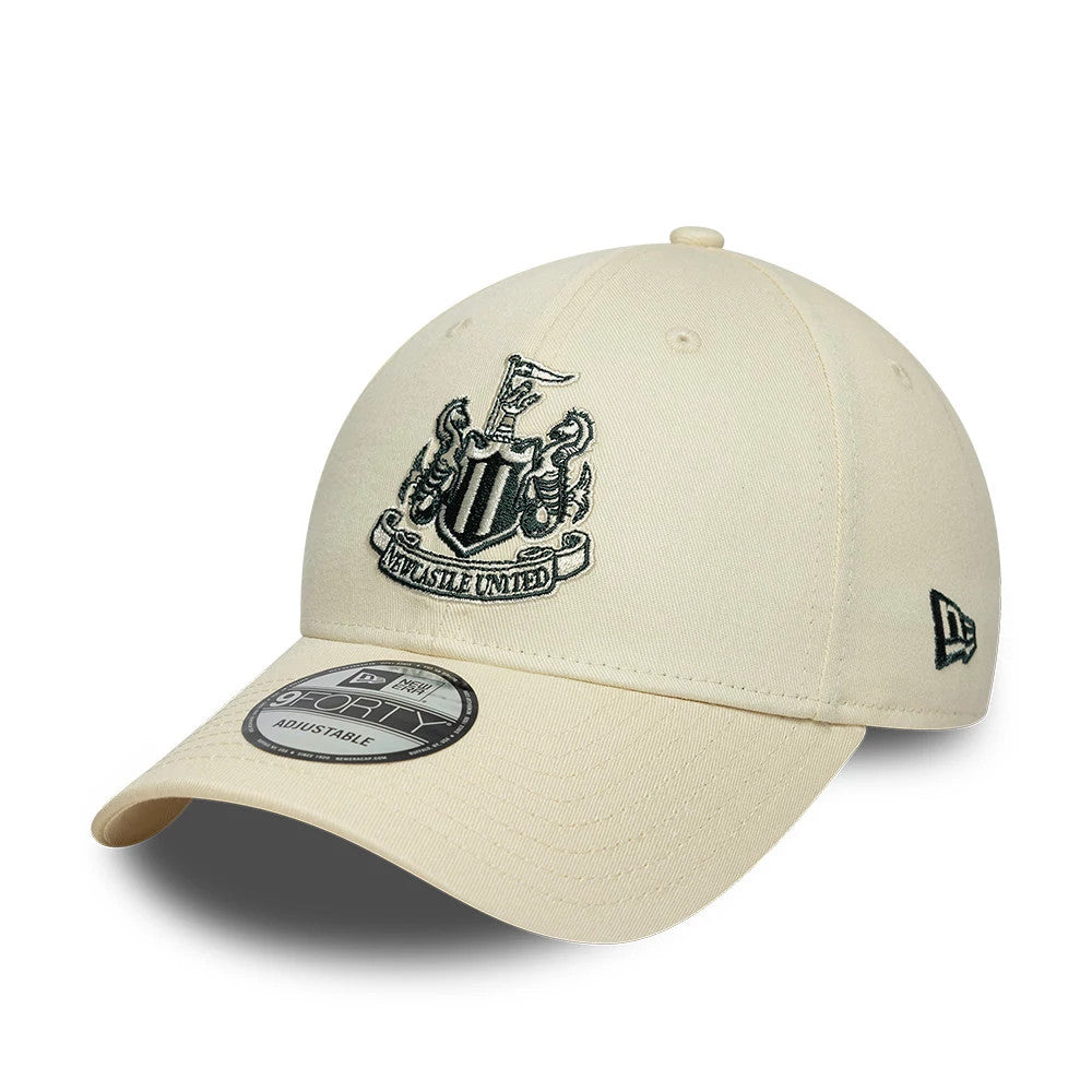 Newcastle United FC Cream New Era 9FORTY Adjustable Cap, three-quarter view showing the black embroidered Newcastle United crest on the front panels, a 9FORTY size sticker on the curved cream visor, and the New Era flag logo on the left side.