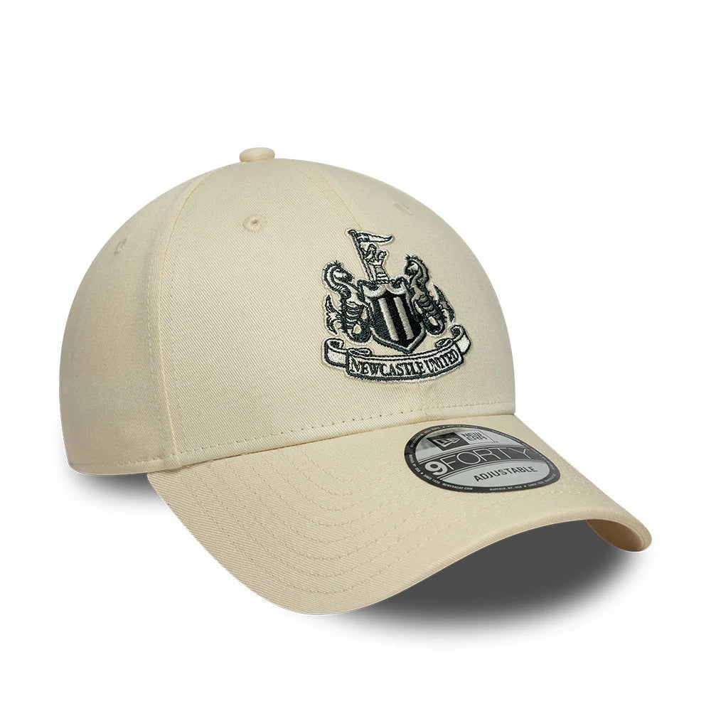 Newcastle United FC Cream New Era 9FORTY Adjustable Cap, three-quarter view showing the embroidered black and white club crest on the front panel, with a matching cream curved visor and a 9FORTY size sticker on the visor.