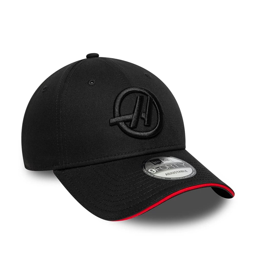TGR Haas F1 Team Cotton Black New Era 9FORTY Adjustable Cap, three-quarter view showing the black raised embroidered Haas logo on the front panel, the black visor with a red edge accent, and the 9FORTY size sticker on the visor.