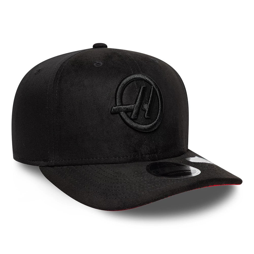 TGR Haas F1 Team Suede Black New Era 9SEVENTY Stretch Snap Adjustable Cap, three-quarter view showing a black raised embroidered team logo on the front panel, black flat visor with 9SEVENTY size sticker, and red undervisor edge.