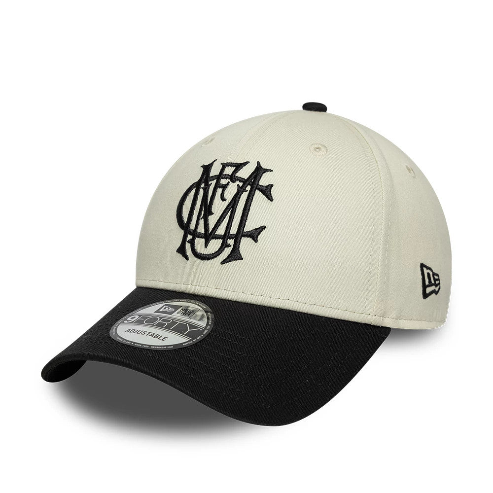 Manchester United FC Monogram Cream & Black New Era 9FORTY Adjustable Cap, three-quarter view showing the black monogram embroidered on the cream front panel, black curved visor with 9FORTY size sticker, and New Era flag logo on the left side.