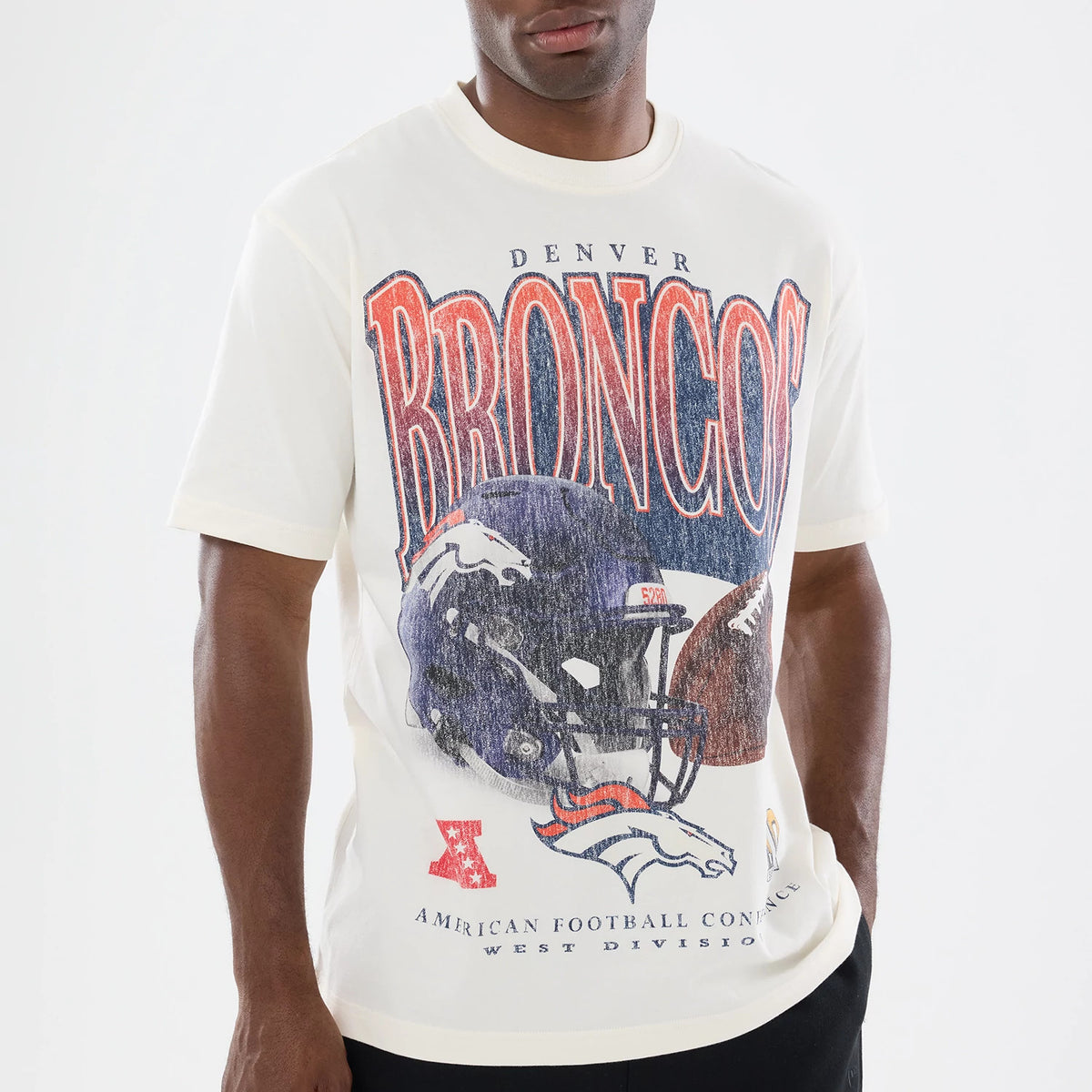 New Era Denver Broncos NFL Sport Classic Cream T-Shirt, front view on-model showcasing large distressed Broncos lettering across the chest, a blue and orange football helmet graphic beneath, and a printed Denver Broncos logo at the bottom.