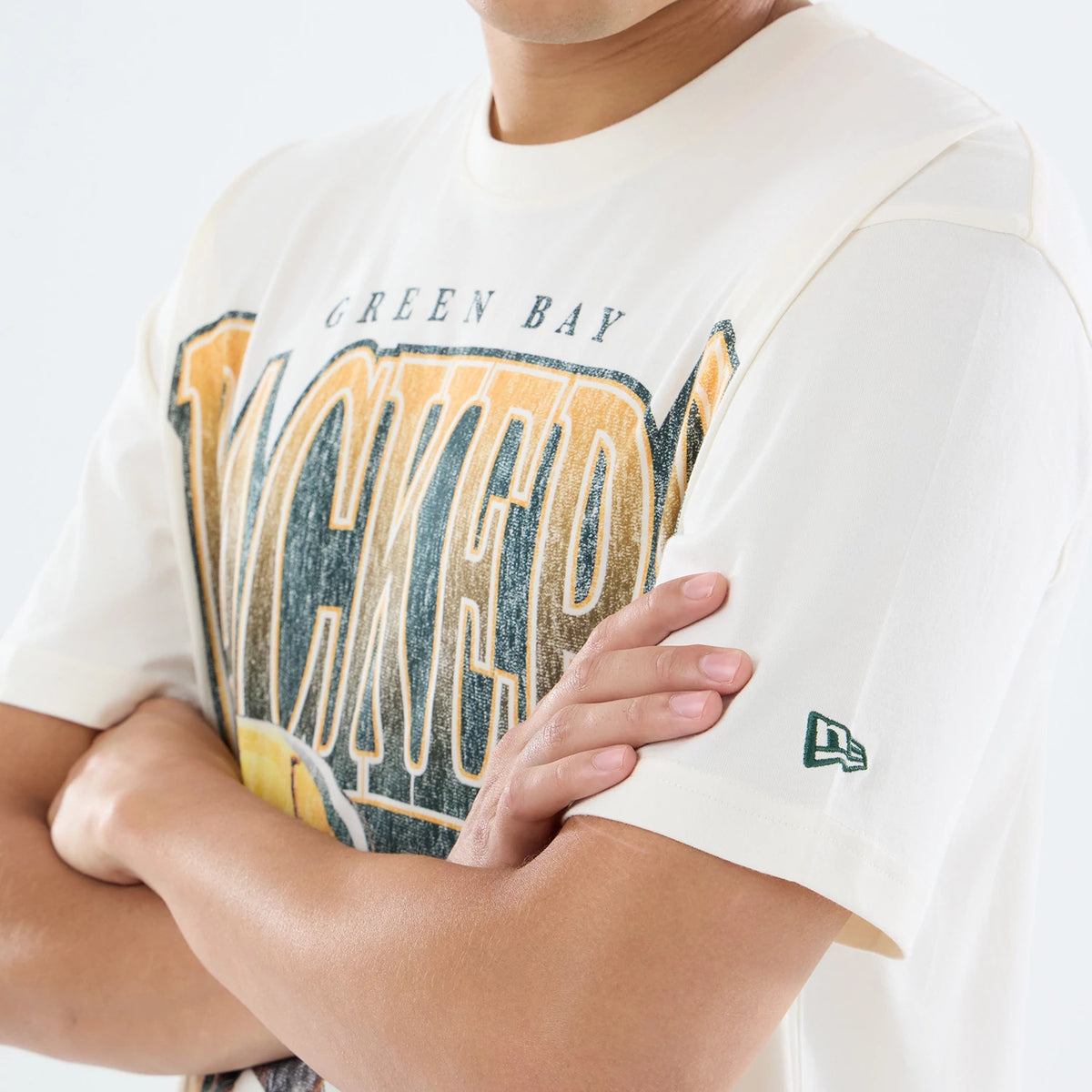 New Era Green Bay Packers NFL Sport Classic Cream T-Shirt, front view showing a PACKERS graphic in gold and black across the chest, with GREEN BAY lettering above, and an embroidered New Era logo on the left sleeve, worn by a model.