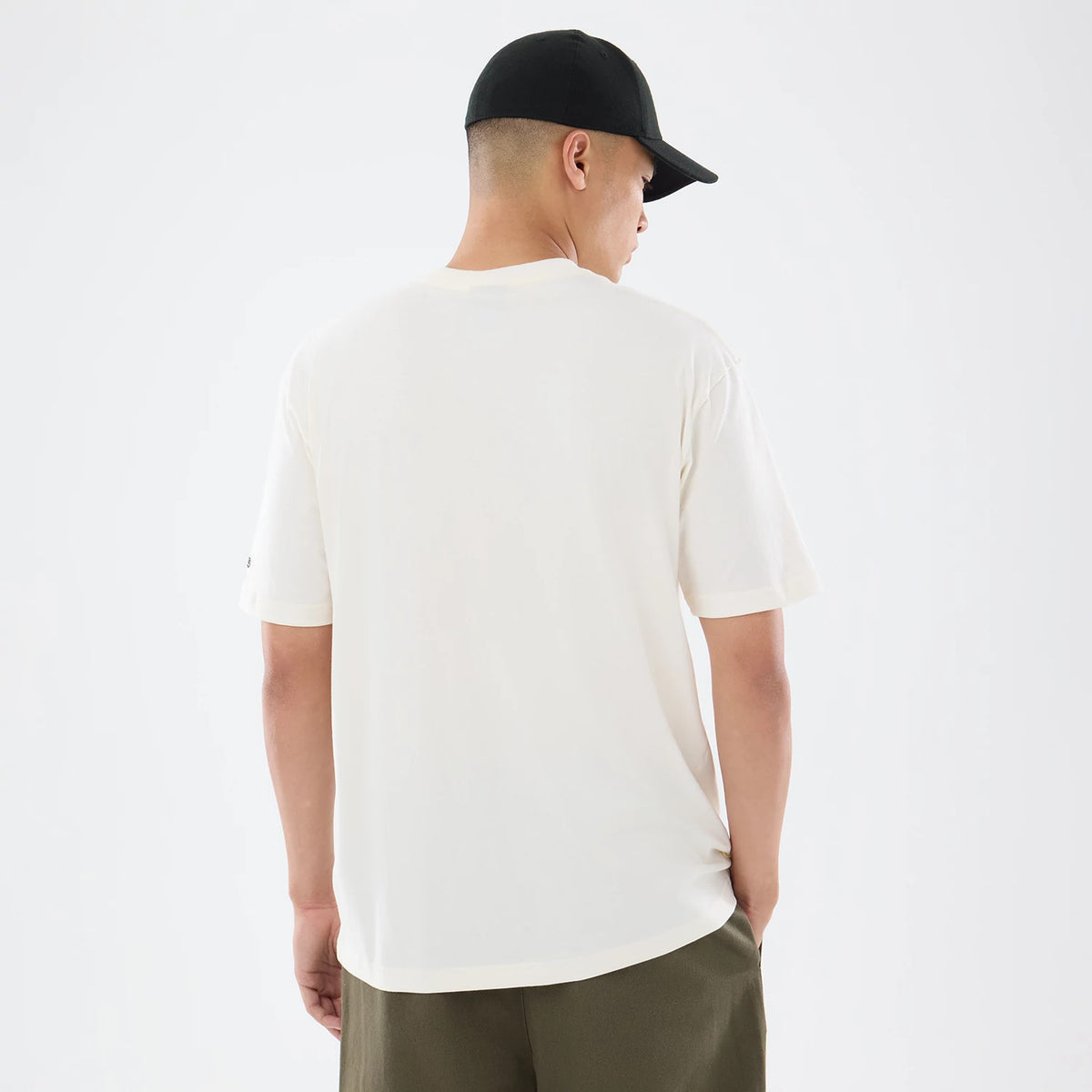 New Era Pittsburgh Steelers NFL Sport Classic Cream T-Shirt, back view on a model wearing dark trousers and a black cap, highlighting the clean cream surface with short sleeves and a small embroidered New Era logo on the left sleeve edge.