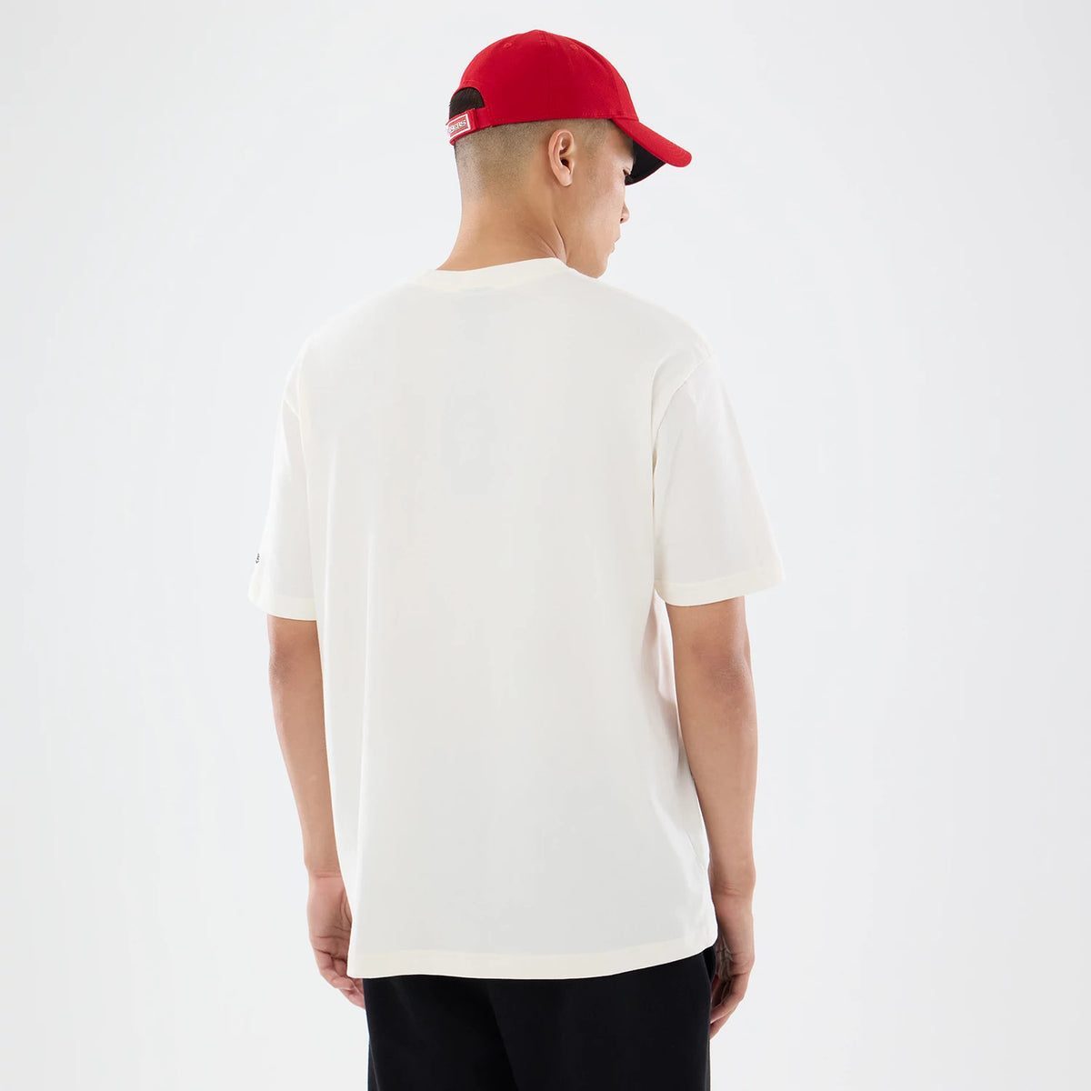 New Era San Francisco 49ers NFL Sport Classic Cream T-Shirt, back view on a model wearing a red cap, highlighting the plain cream design without graphic details, short sleeves, and a small embroidered New Era logo on the left sleeve.