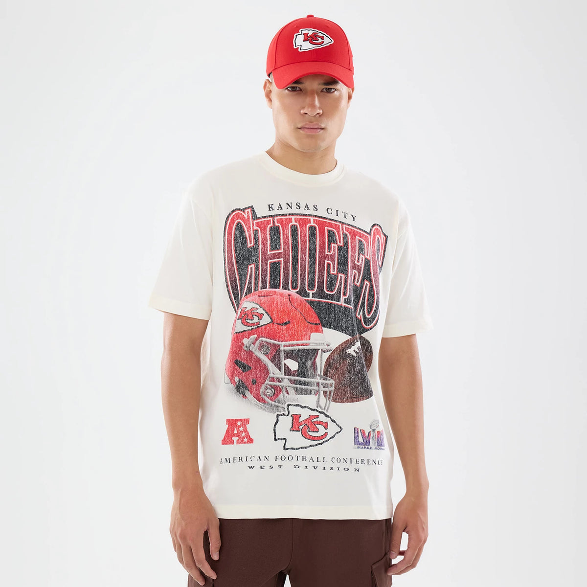New Era Kansas City Chiefs NFL Sport Classic Cream T-Shirt, front view on a model featuring Chiefs lettering across the chest, a large graphic of a football helmet below, and an embroidered New Era logo centred above in red.