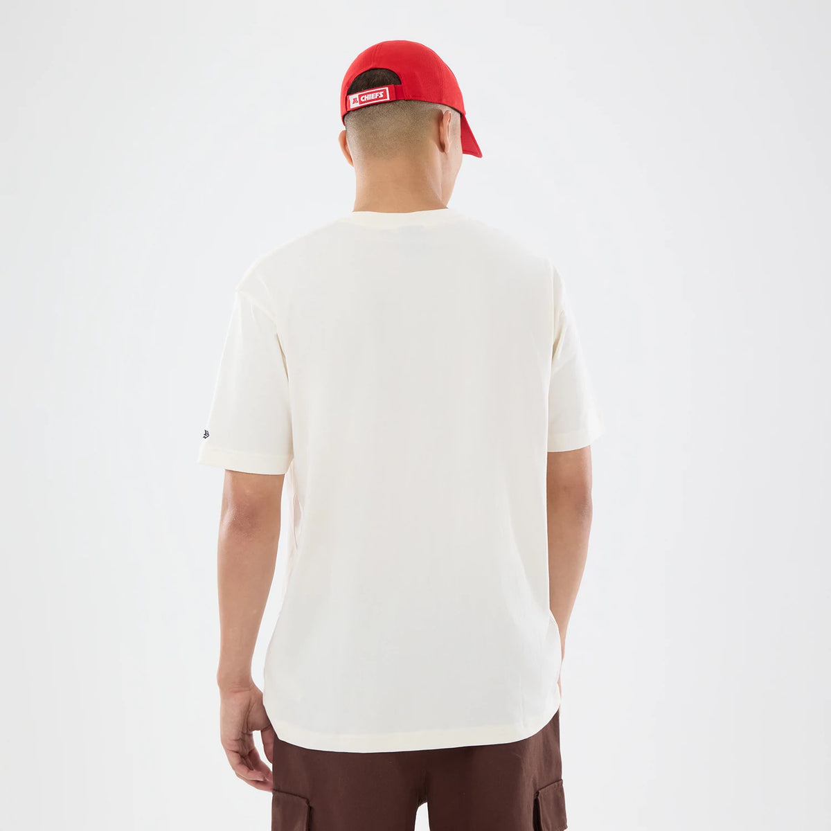 New Era Kansas City Chiefs NFL Sport Classic Cream T-Shirt, back view on a model wearing a red cap, showing a clean cream design with a simple silhouette, and an embroidered New Era logo on the left sleeve near the hem.