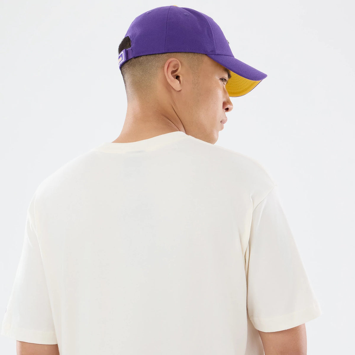 New Era Minnesota Vikings NFL Sport Classic Cream T-Shirt, back view on a model wearing a purple and yellow cap, highlighting the plain cream fabric of the T-shirt, and short sleeves with a simple crew neck design.