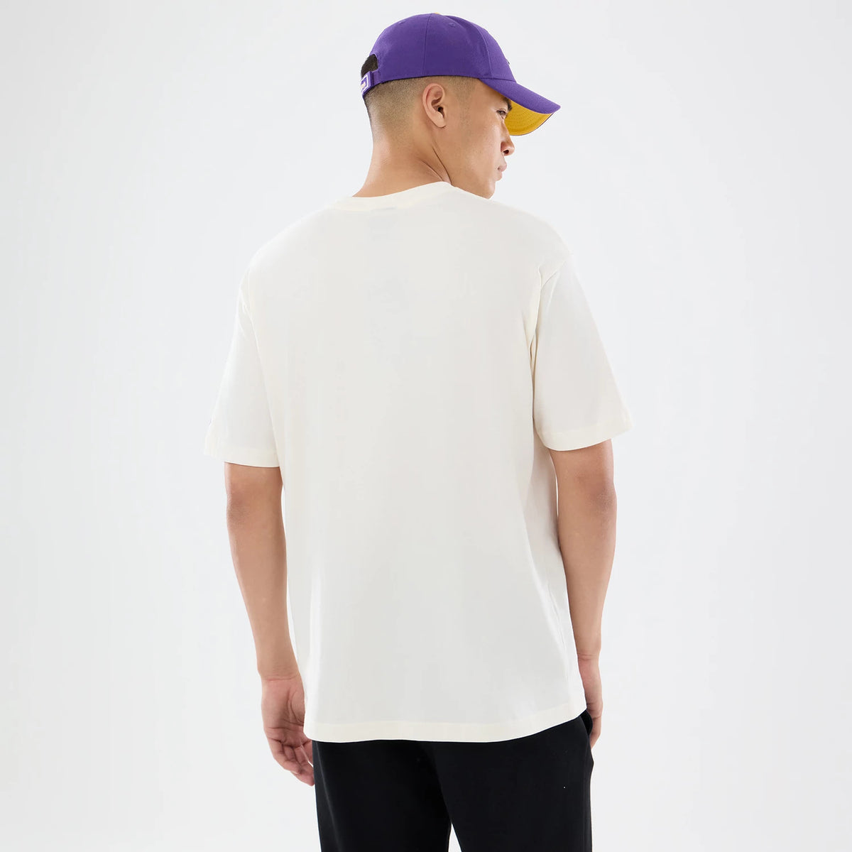 New Era Minnesota Vikings NFL Sport Classic Cream T-Shirt, back view on a model, highlighting the plain cream back with short sleeves, complemented by a purple cap featuring an embroidered New Era logo and a contrast yellow underbill.