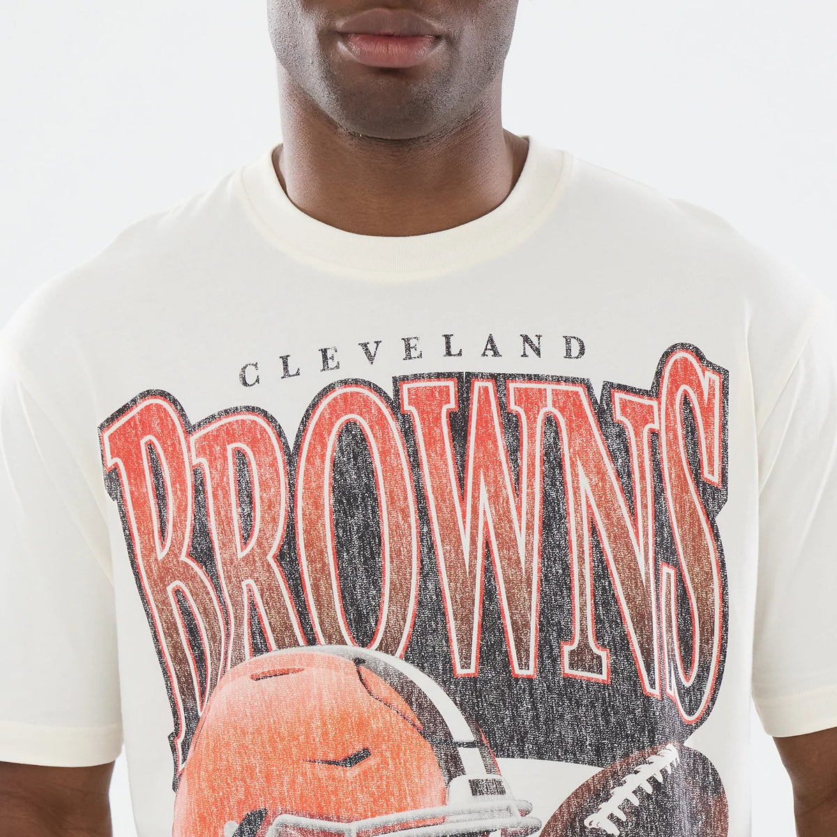 New Era Cleveland Browns NFL Sport Classic Cream T-Shirt, front view displaying distressed Cleveland Browns lettering and a large graphic of a football helmet, worn by a model with short sleeves showing the cream fabric and a relaxed fit neckline.