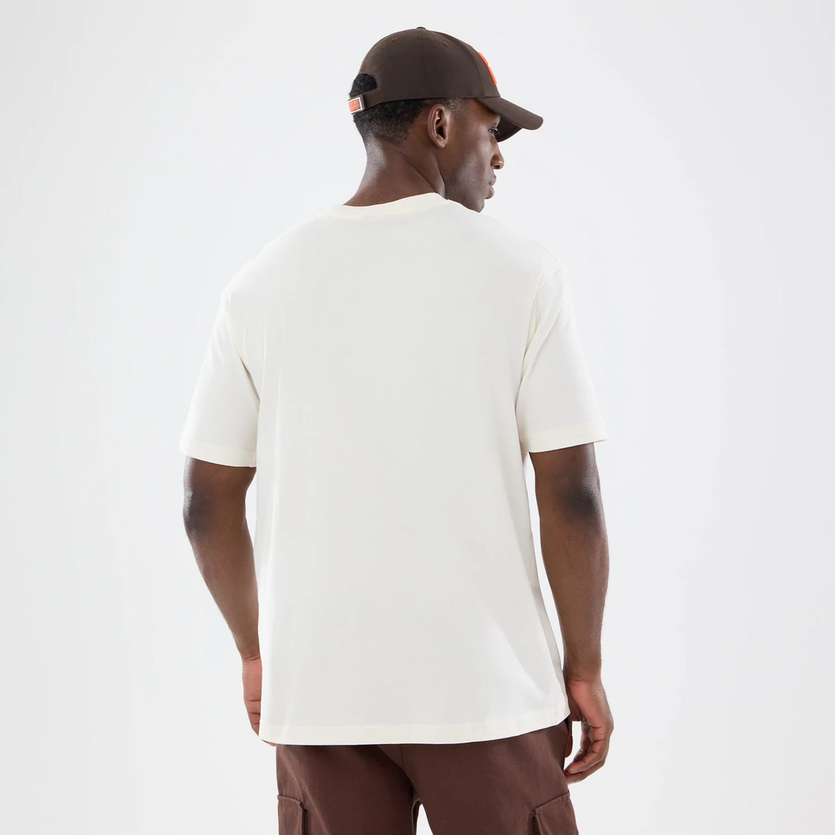 New Era Cleveland Browns NFL Sport Classic Cream T-Shirt, back view on a model wearing brown trousers and a matching cap, showing the plain cream back of the t-shirt with short sleeves and a relaxed fit, highlighting the minimalistic design.