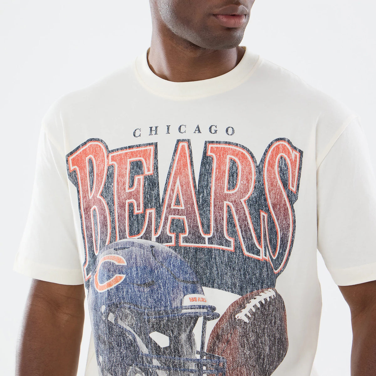 New Era Chicago Bears NFL Sport Classic Cream T-Shirt, front view showing large faded BEARS lettering in orange and navy across the chest, a football helmet graphic below with a logo, and a football image to the side.