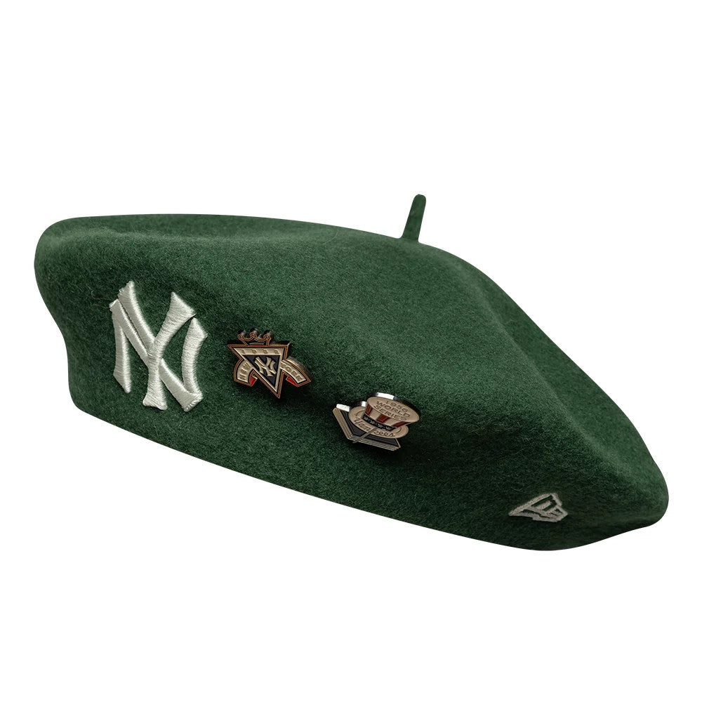 New Era New York Yankees MLB Cooperstown Pin Dark Green Beret, side view showcasing the dark green beret with a prominent white embroidered Yankees logo on the front, two decorative pins next to it, and a small embroidered New Era logo on the side.