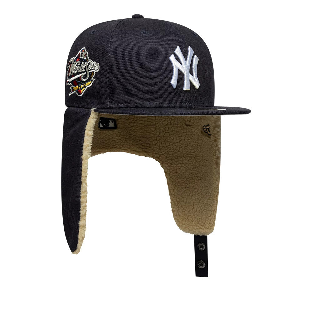 New York Yankees MLB World Series Navy Dogear New Era 59FIFTY Fitted Cap, side view showing the white embroidered NY logo on the front panel, a World Series patch on the side, and extended dogear flaps with beige fleece lining.