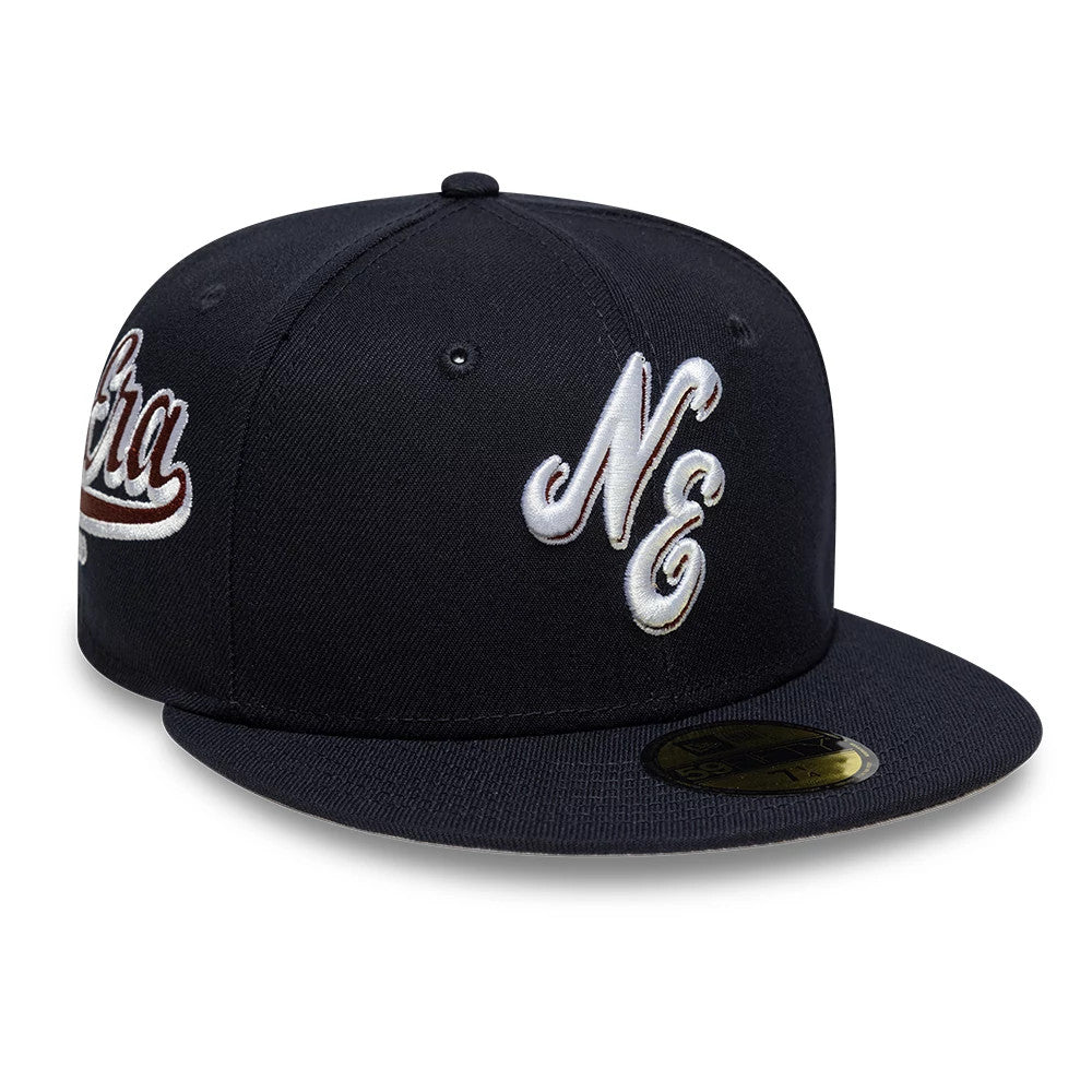 New Era Heritage Script Navy 59FIFTY Fitted Cap, three-quarter view showing the raised white NE embroidery on the front panel, a flat visor with a gold 59FIFTY size sticker, and the Era script in white and red thread on the side.