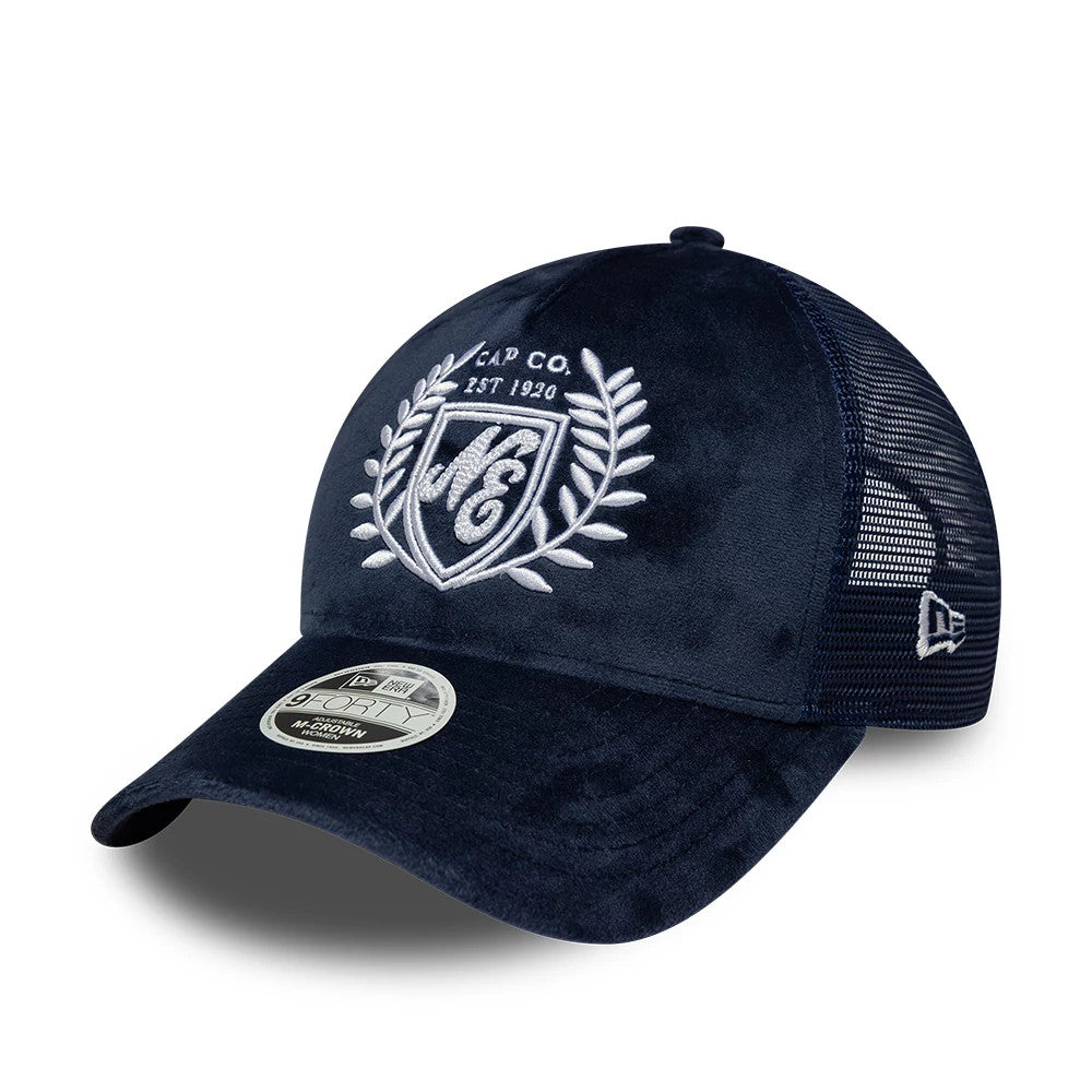 Womens New Era Velour Navy 9FORTY M-Crown A-Frame Trucker Adjustable Cap, three-quarter view showing the white embroidered shield and laurel design on the front panel, a curved navy velour visor with a 9FORTY size sticker, and mesh back panels.