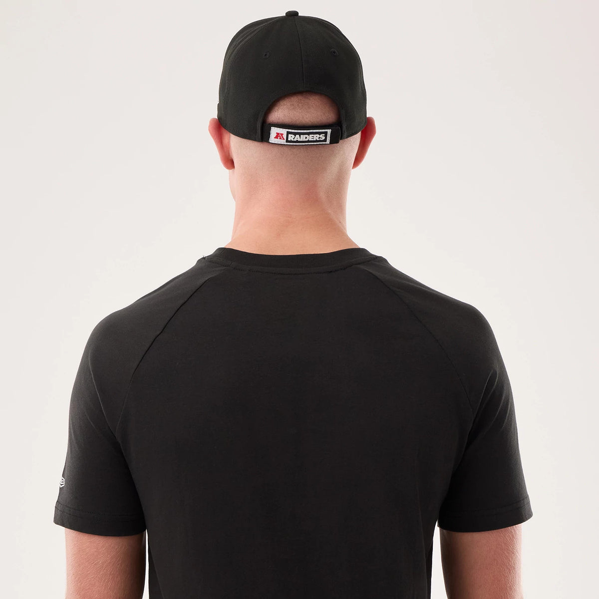 New Era Las Vegas Raiders NFL Sideline 2026 Black T-Shirt, back view on a model with a matching cap showing a plain black back with no graphics. The cap features a contrast white and black Raiders label on the back strap.
