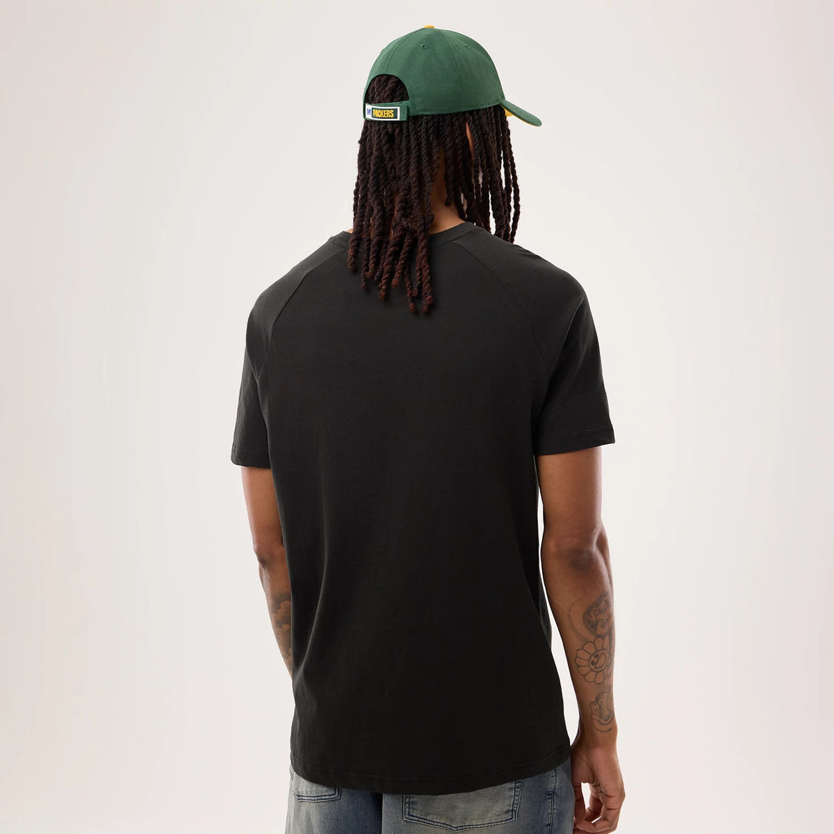 New Era Green Bay Packers NFL Sideline 2026 Black T-Shirt, back view on a model with a seam running across the shoulders, styled casually with blue jeans and a green Packers cap featuring an embroidered team name on the back strap.