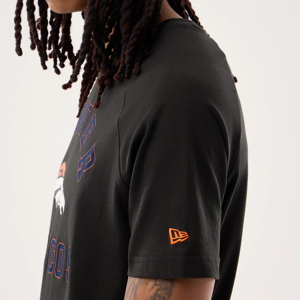 New Era Denver Broncos NFL Sideline 2026 Black T-Shirt, side view on a model showing the embroidered orange New Era logo on the sleeve, the Broncos logo and lettering on the chest, and a relaxed fit.
