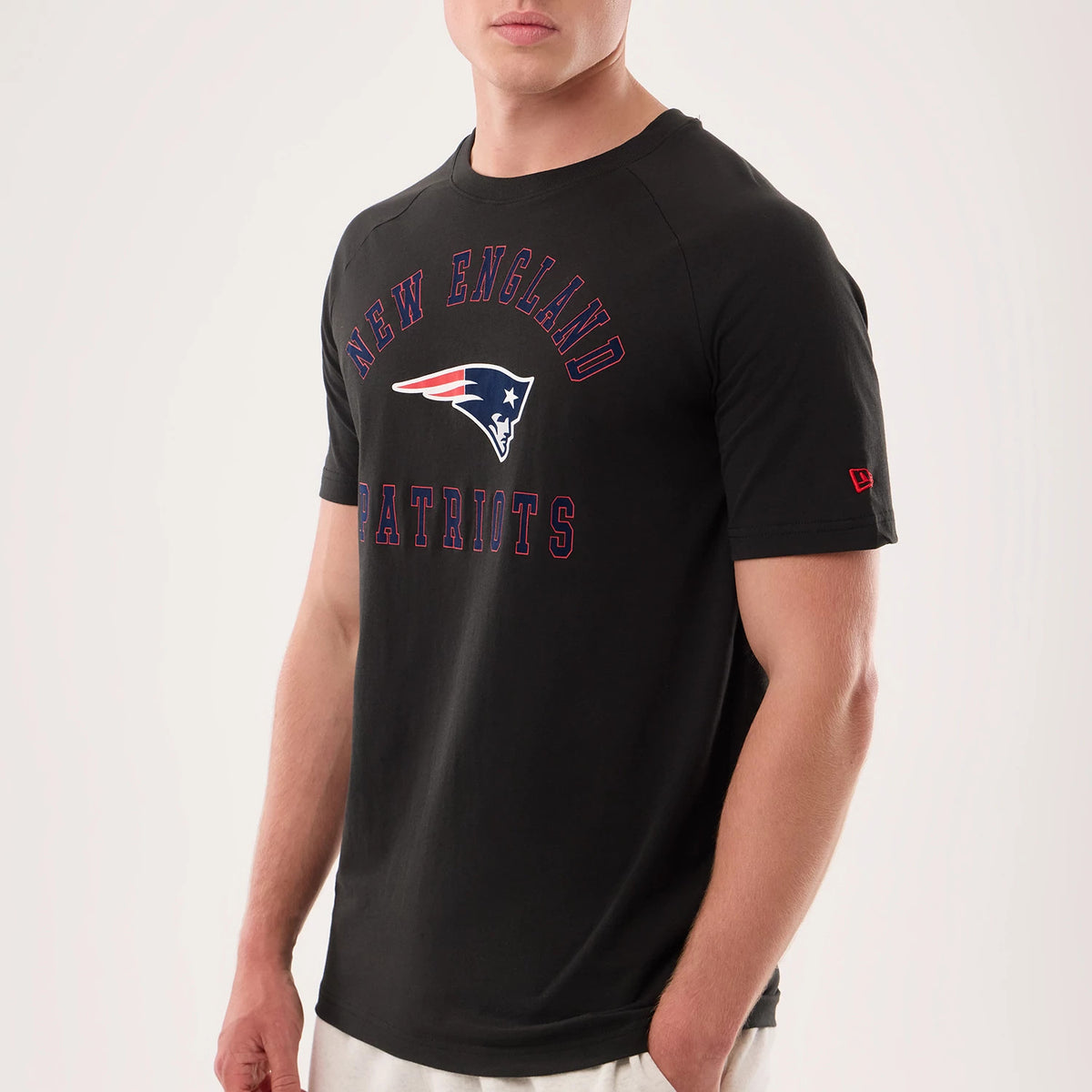 New Era New England Patriots NFL Sideline 2026 Black T-Shirt, three-quarter view showcasing the black tee with New England lettering and Patriots logo printed on the chest, emphasising the red embroidered New Era logo on the left sleeve.